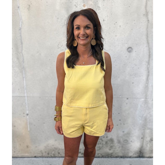 Woman wearing a yellow outfit standing against a textured wall.