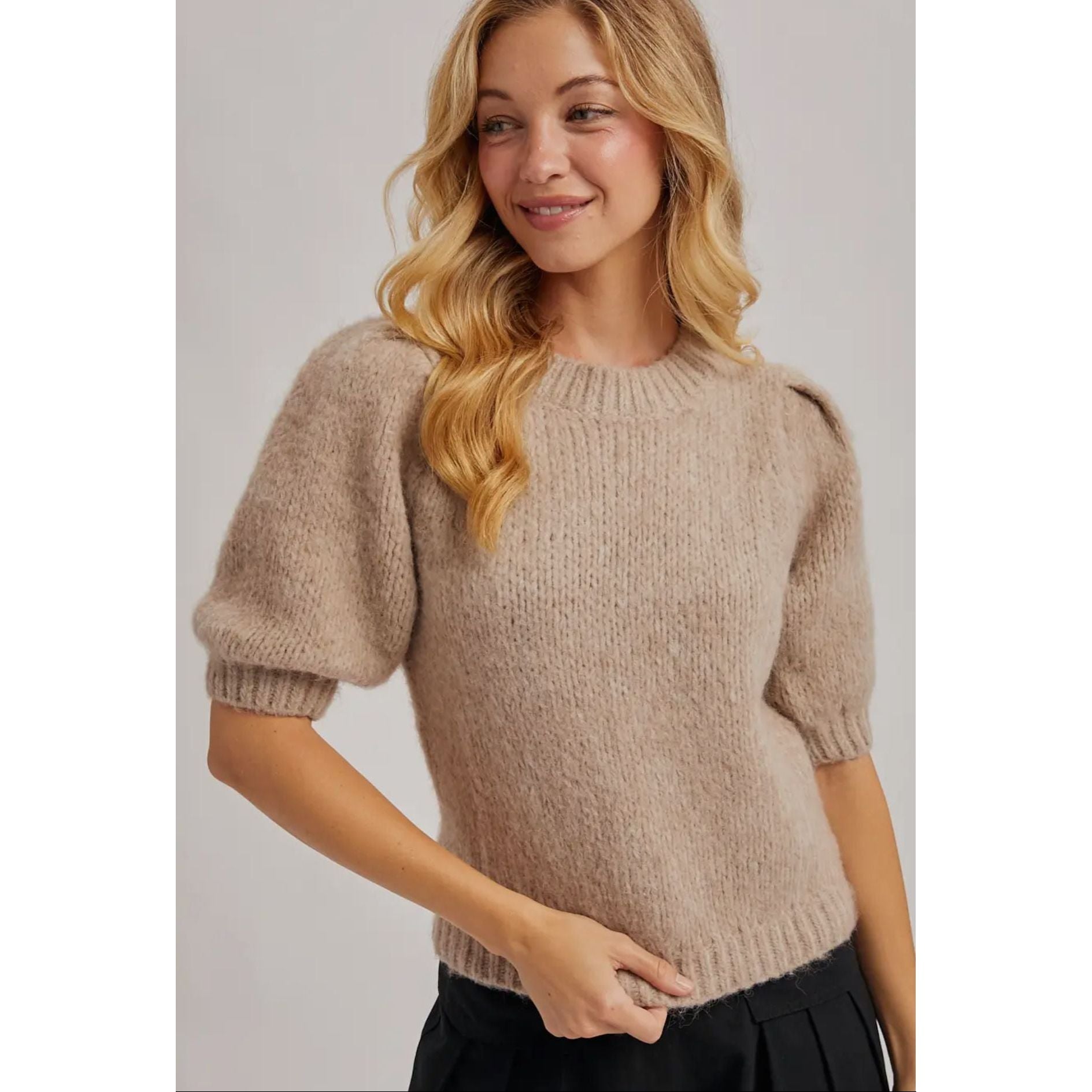 Woman wearing a beige knit sweater against a plain background