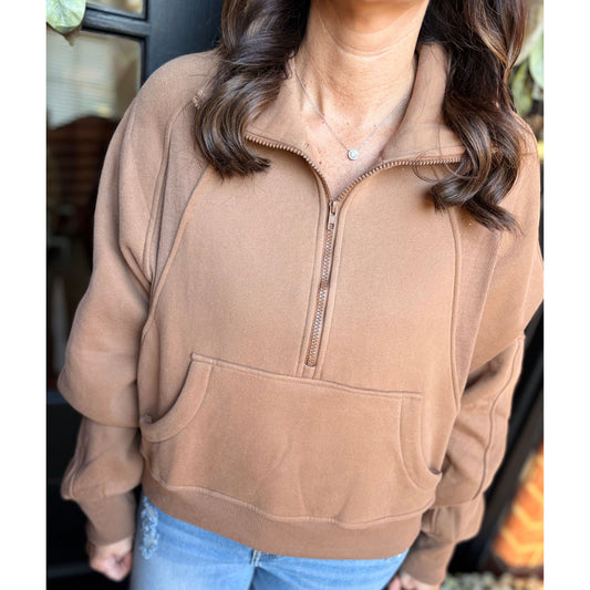 Person wearing a brown half-zip sweatshirt with a blurred background