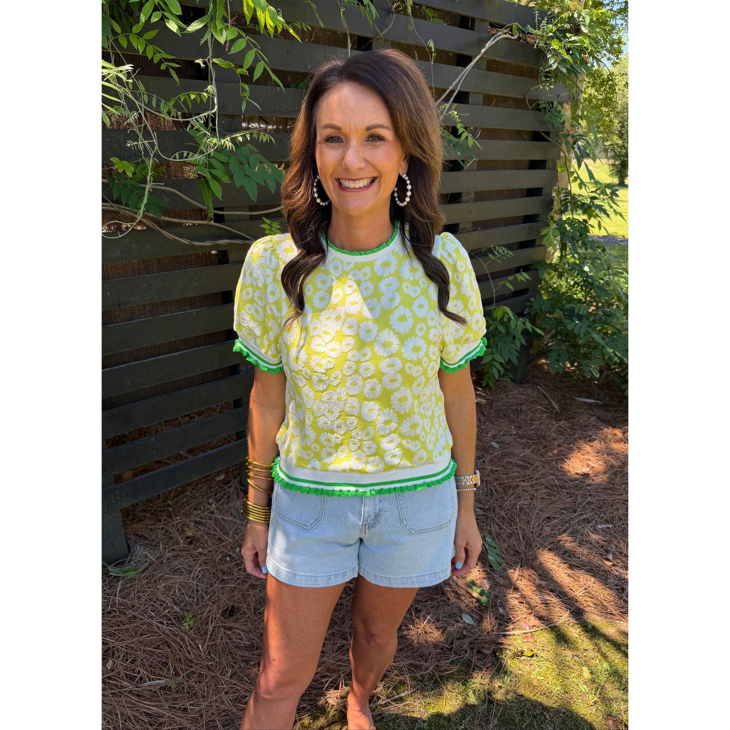 Woman in a green floral dress and light blue shorts sitting on a bench outdoors.