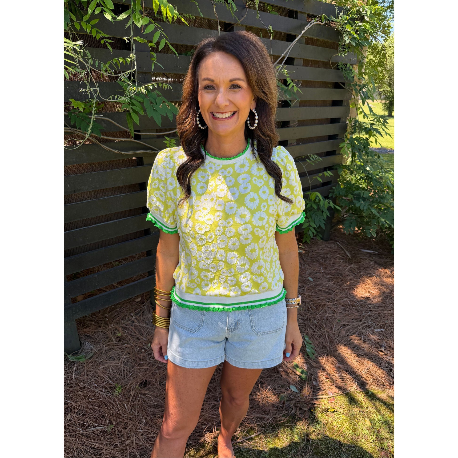 Woman in a green floral dress and light blue shorts sitting on a bench outdoors.