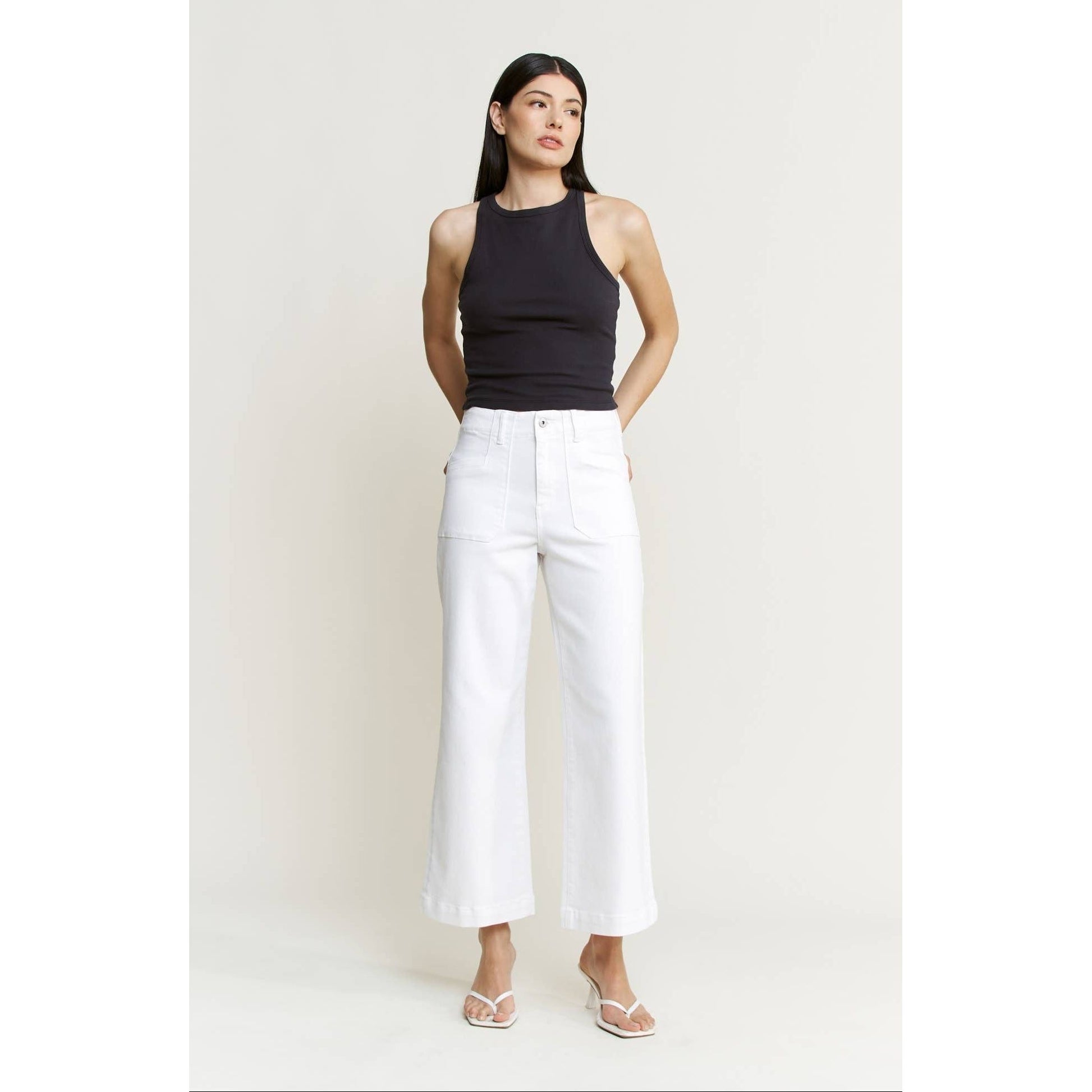 Woman wearing a black sleeveless top and white pants against a light background