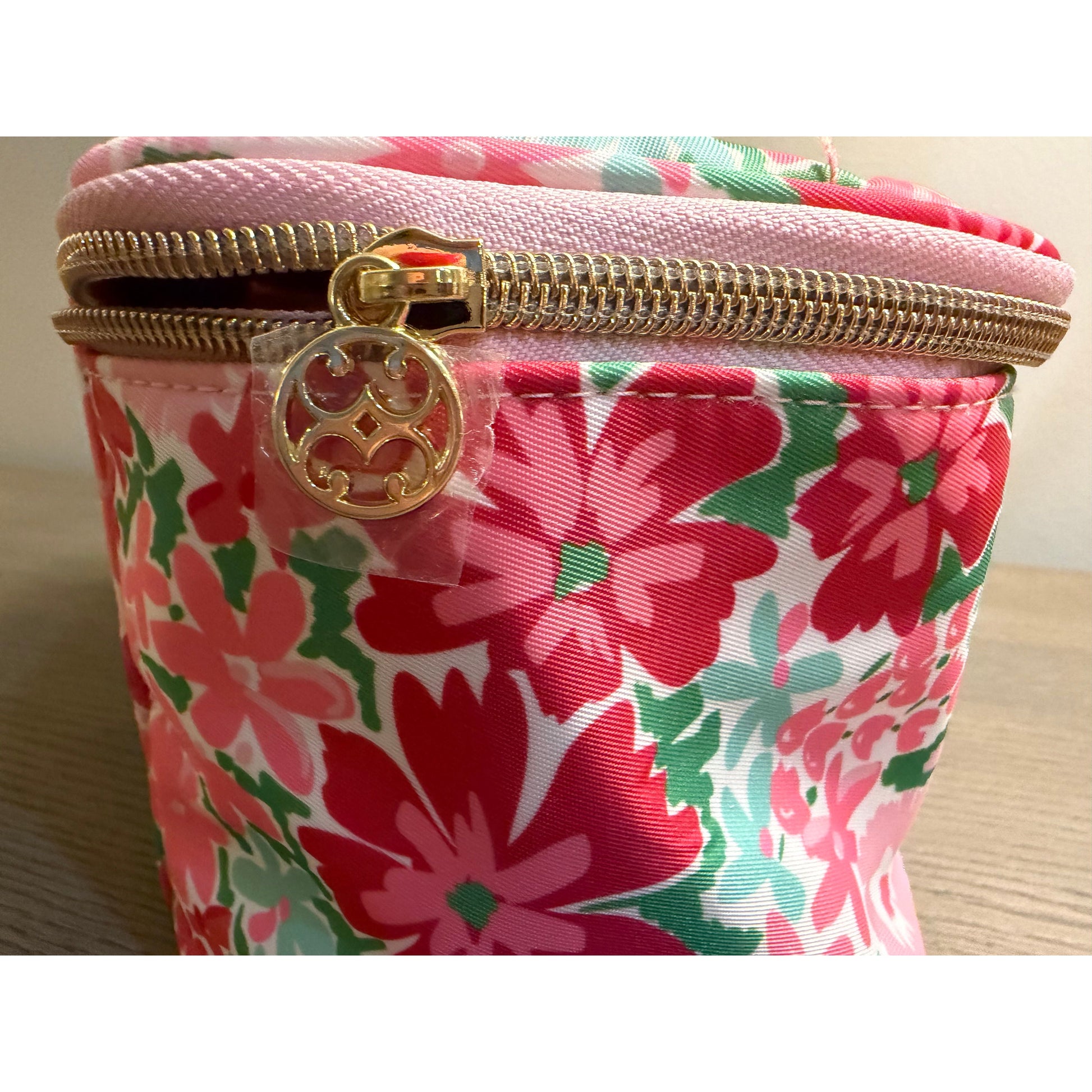 Floral-patterned pouch with gold zipper and logo on a wooden surface