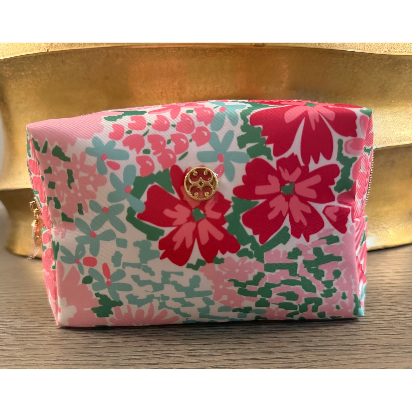 Floral-patterned pouch with a gold logo on a wooden surface