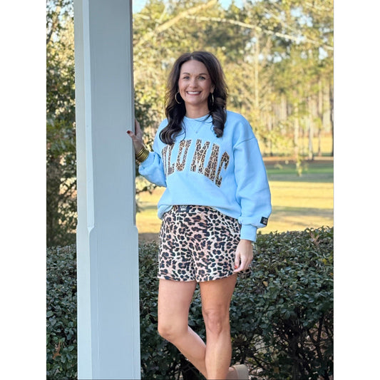 Woman wearing a light blue sweatshirt with 'Welcome' text and a leopard print skirt outdoors.