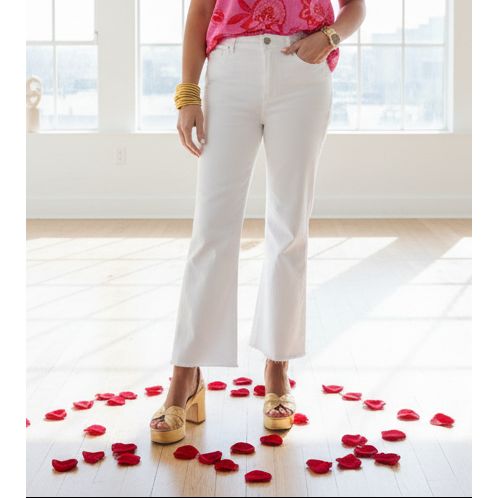 Person wearing a pink top with a floral design, white pants, and gold sandals indoors.