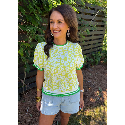 Woman wearing a yellow floral top and white shorts outdoors