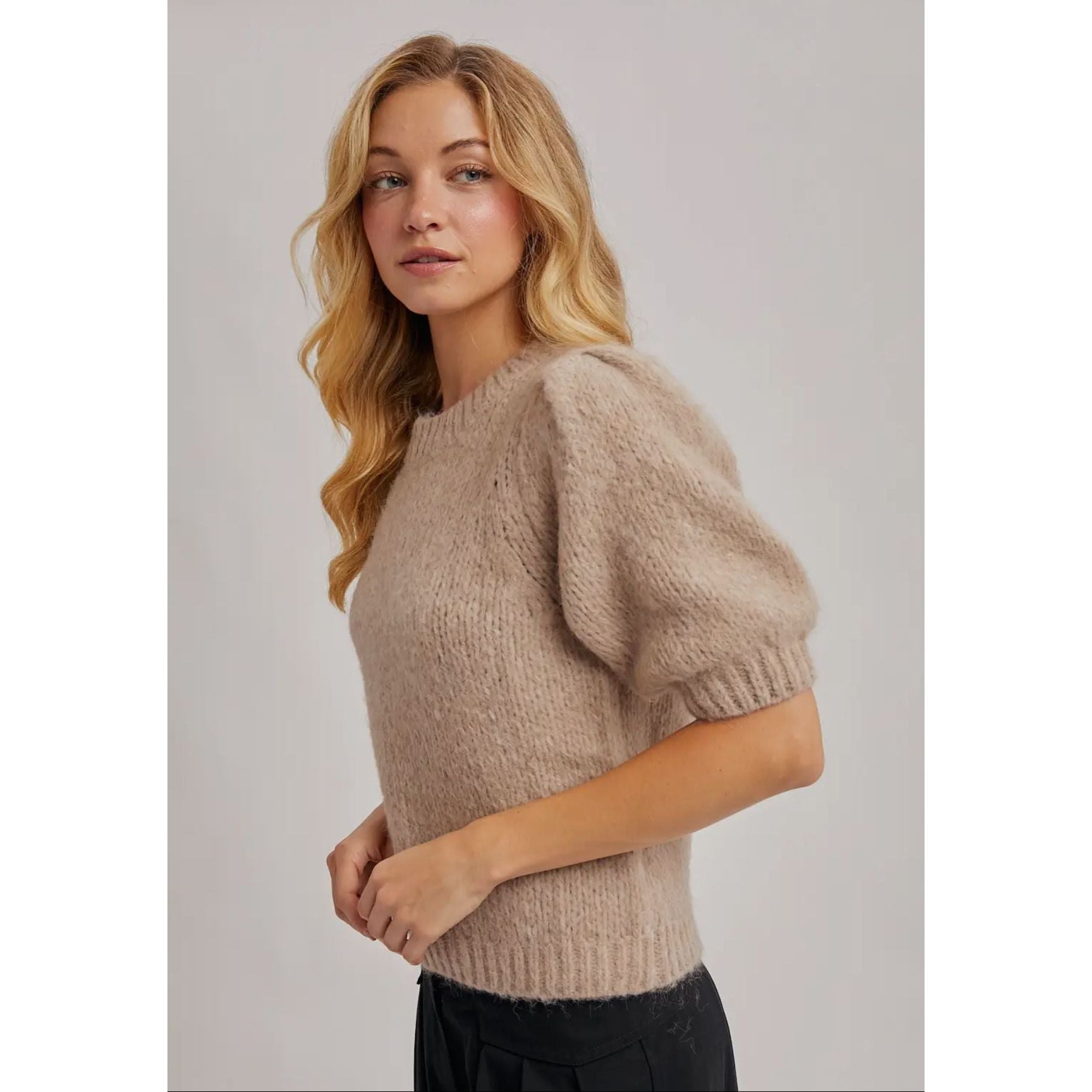 Woman wearing a beige knit sweater against a plain background