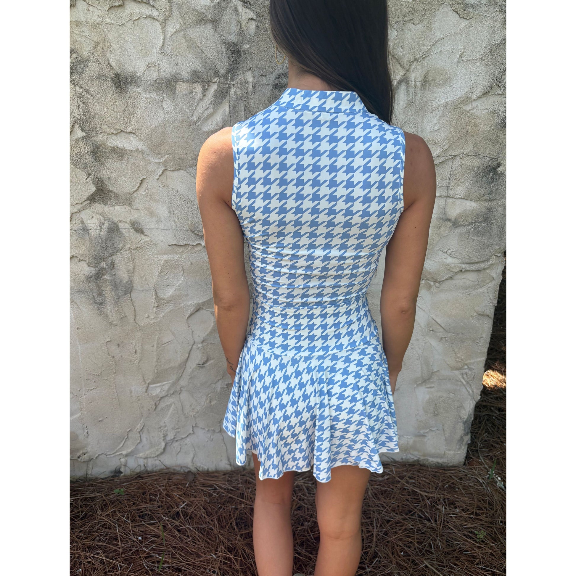 Person wearing a blue and white checkered dress against a stone wall.