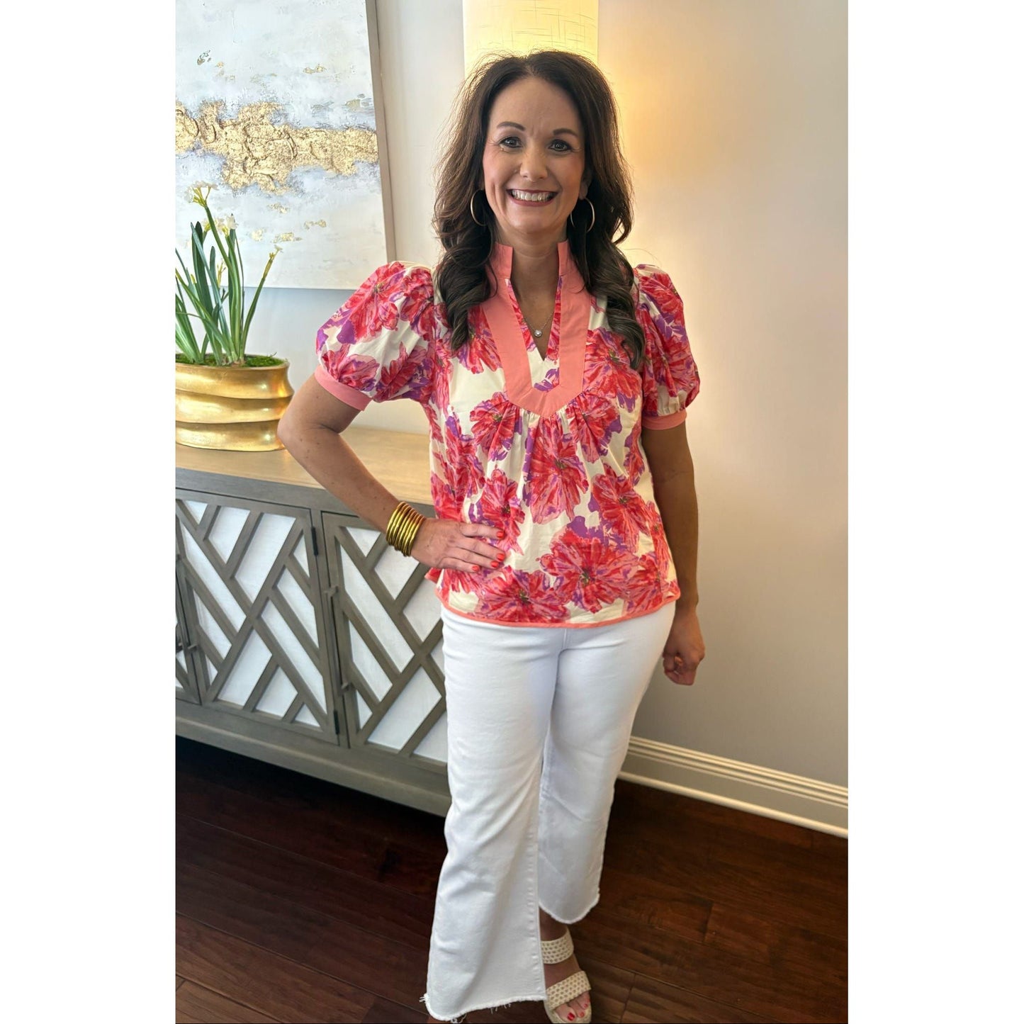 Woman wearing a colorful floral blouse and white pants indoors.