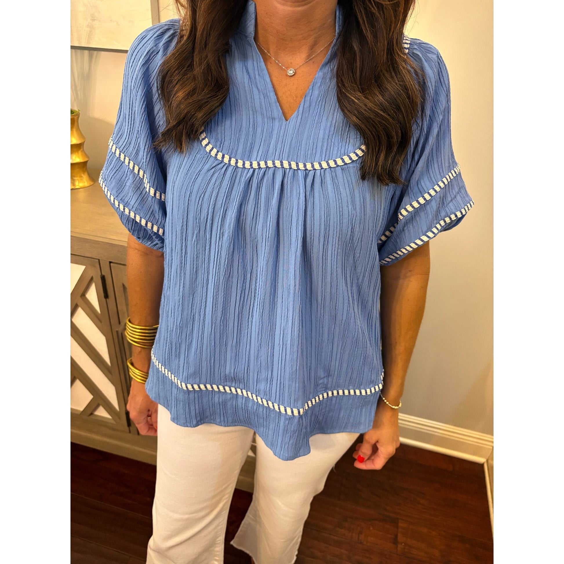 Woman wearing a blue blouse with white trim indoors.