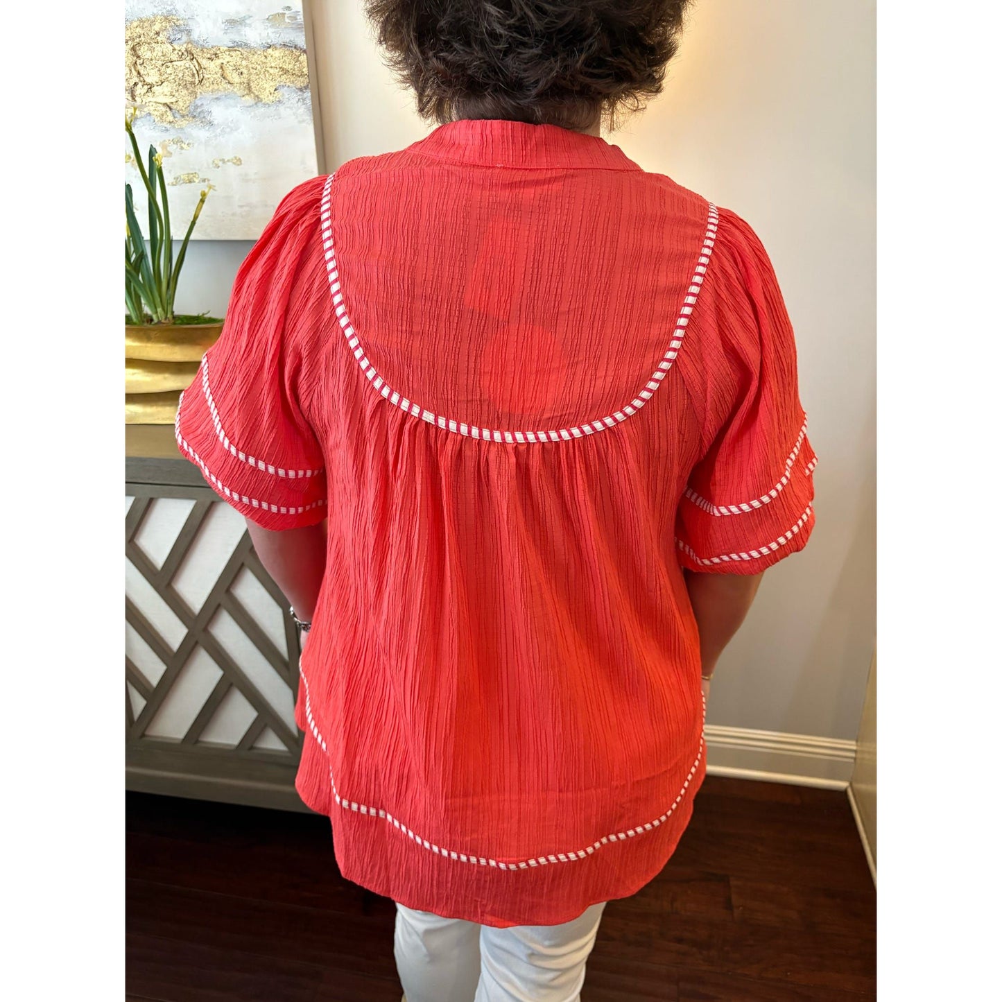 Person wearing a red blouse with white trim in an indoor setting