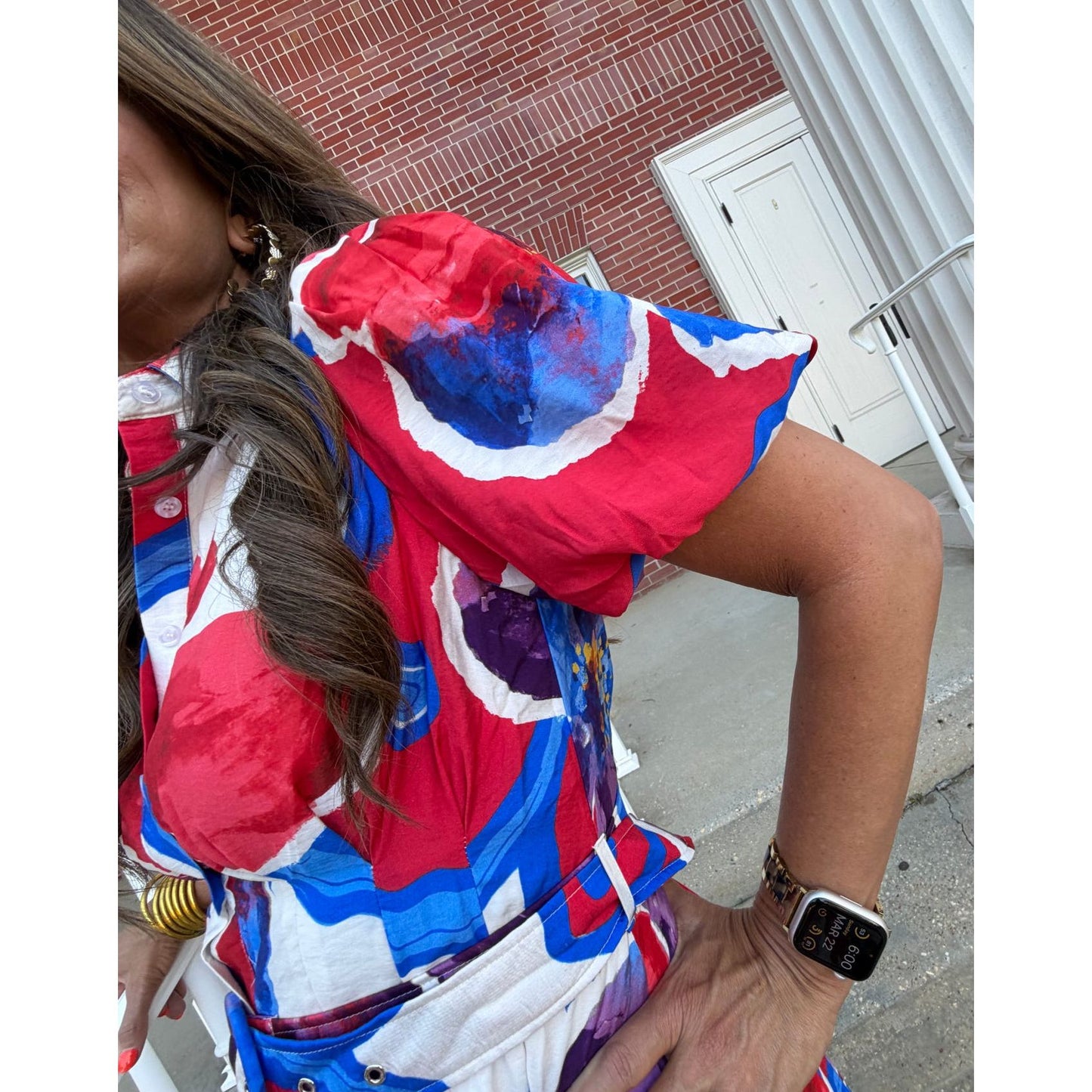 Person wearing a colorful dress with a red, blue, and white pattern on a sidewalk.