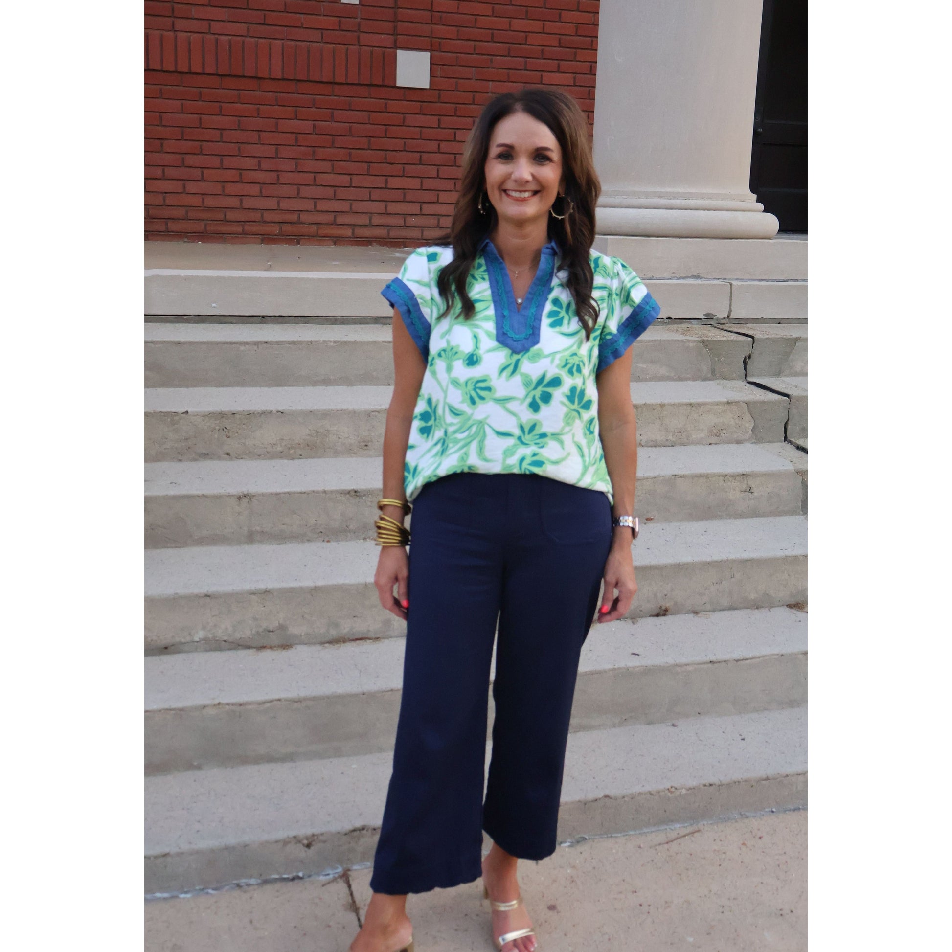 Woman standing on a set of stairs wearing a blue and green top with dark pants.