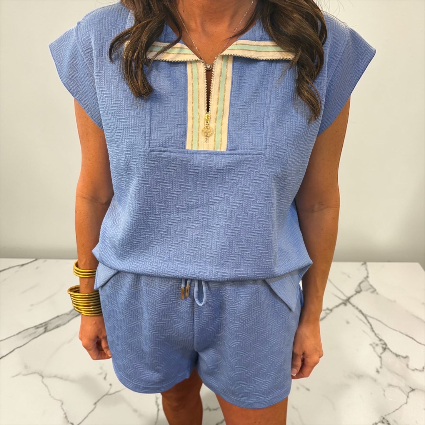 Person wearing a blue outfit with a zipper detail on a marble surface