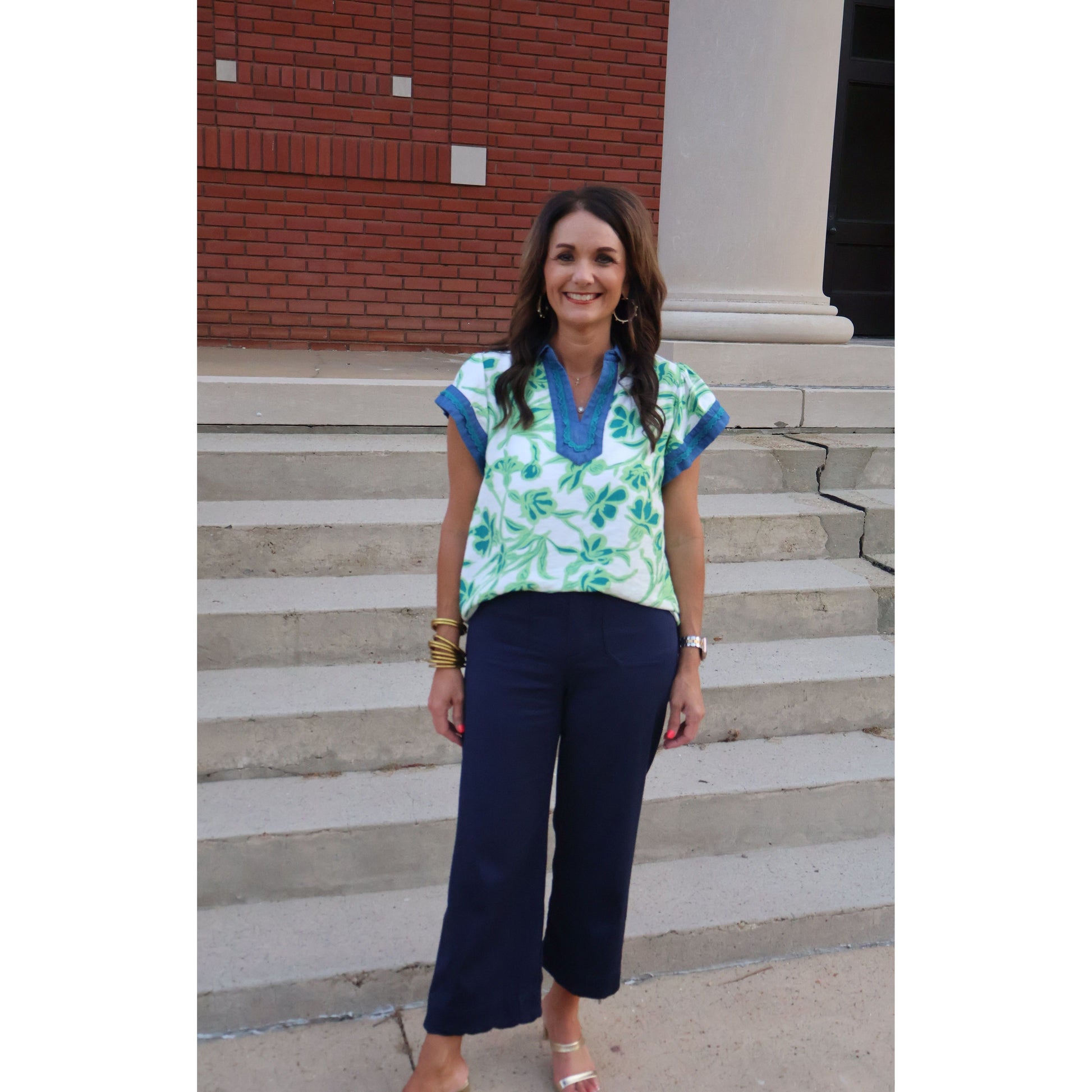 Woman standing on a set of stairs wearing a blue and green top with dark pants.