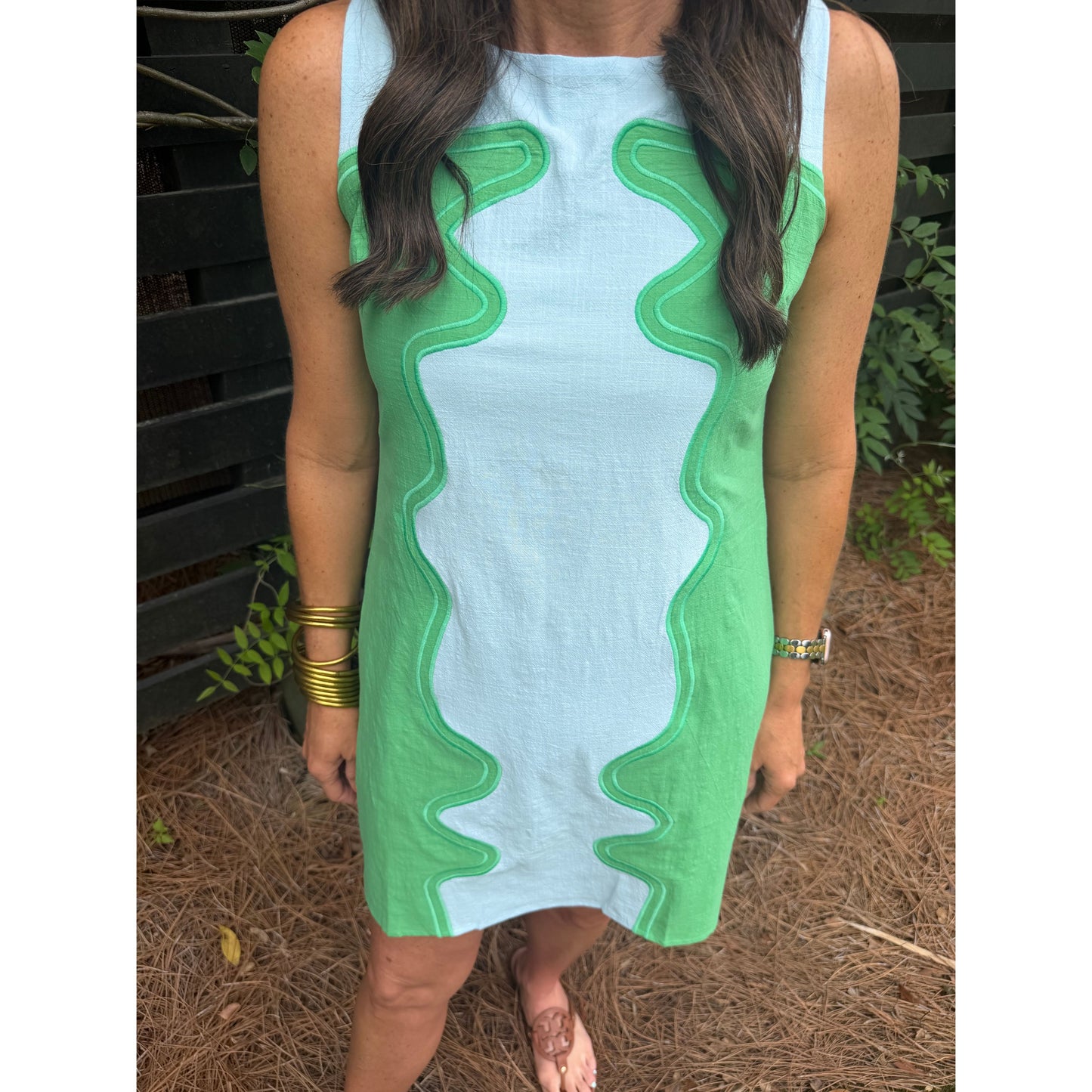 Woman wearing a sleeveless dress with green and white pattern outdoors.