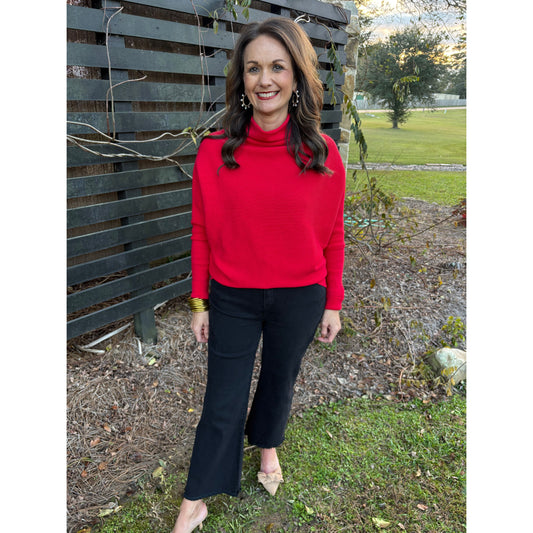 Woman in a red sweater and black pants standing outdoors on a bench.