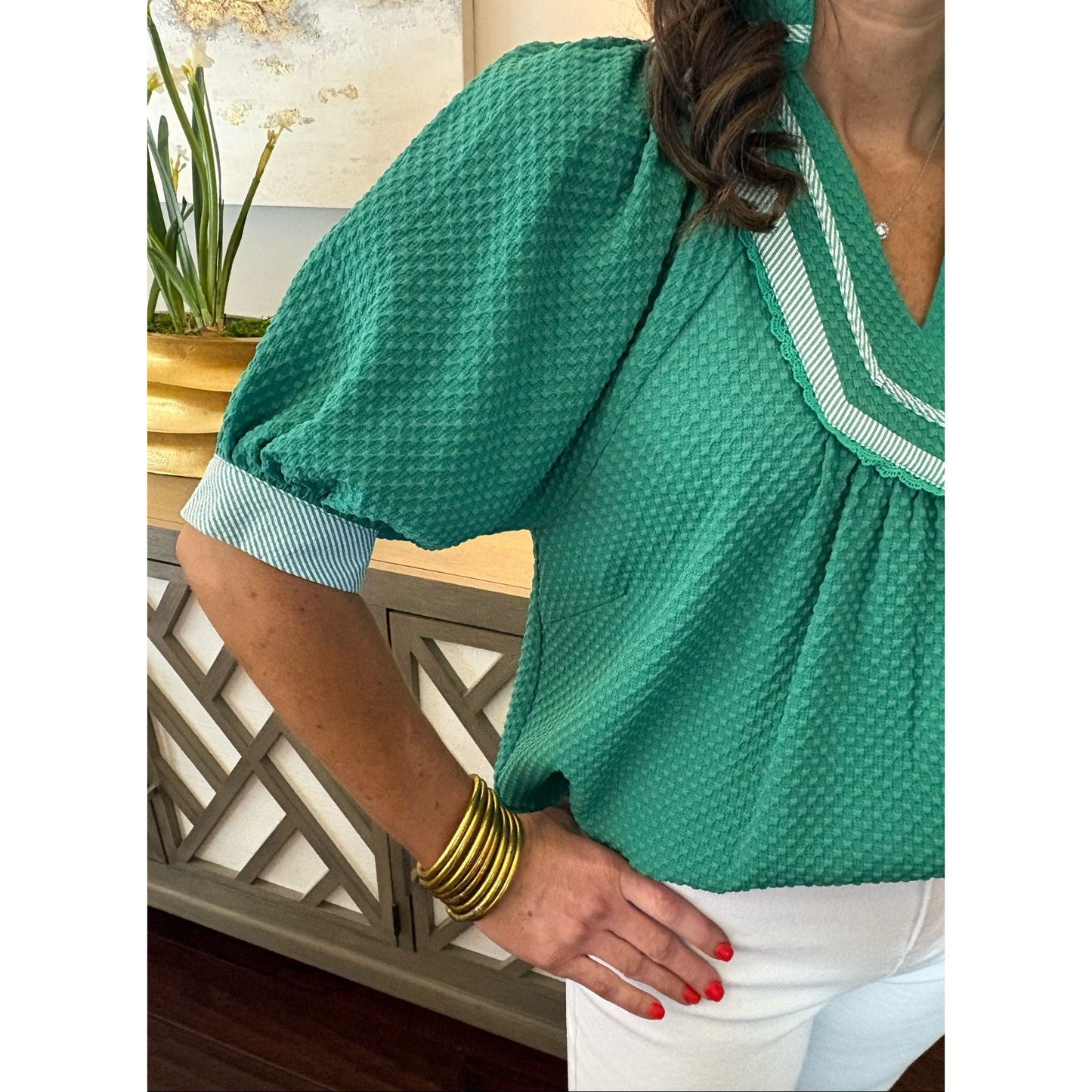 Person wearing a green textured blouse with white trim, sitting on a chair.