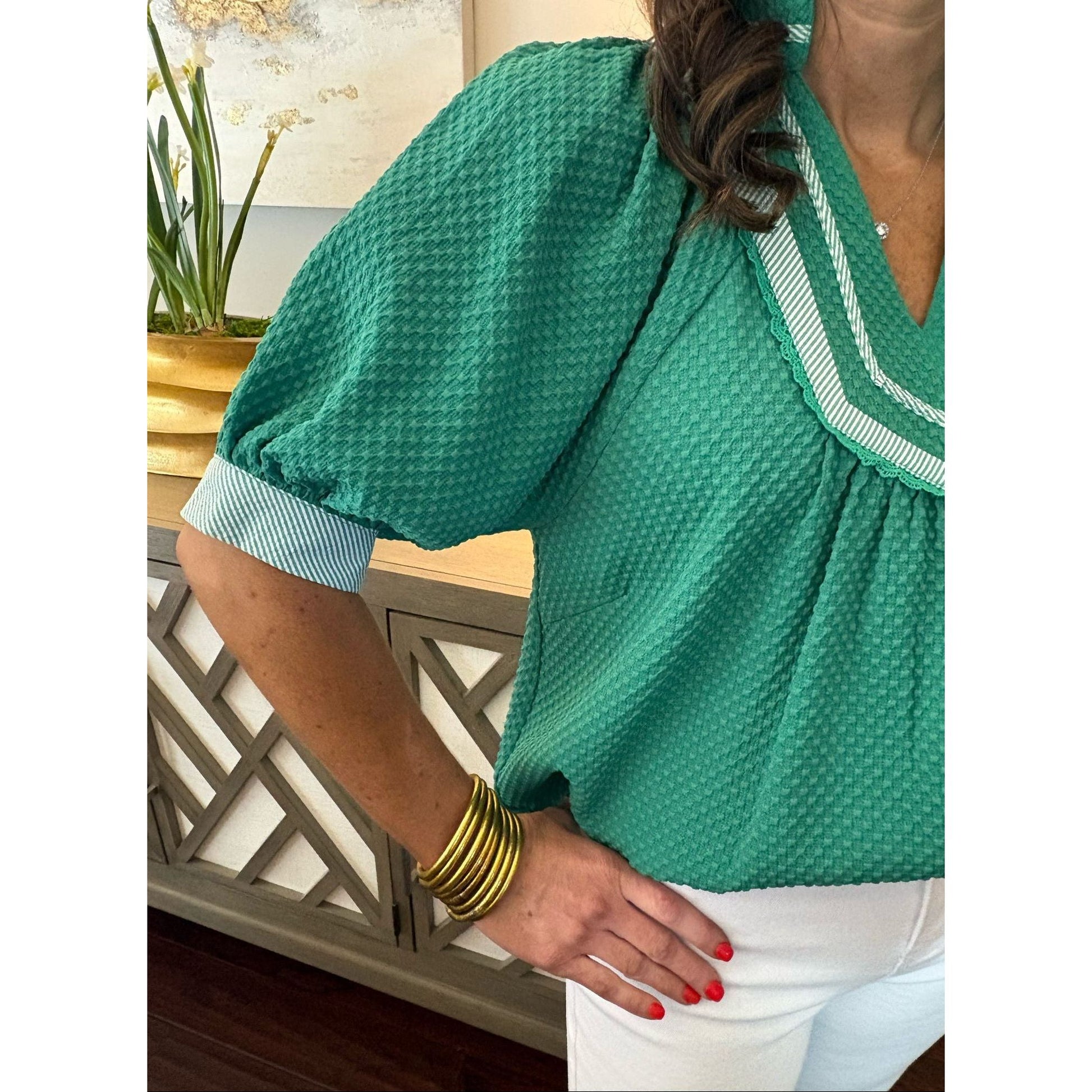 Person wearing a green textured blouse with white trim, sitting on a chair.