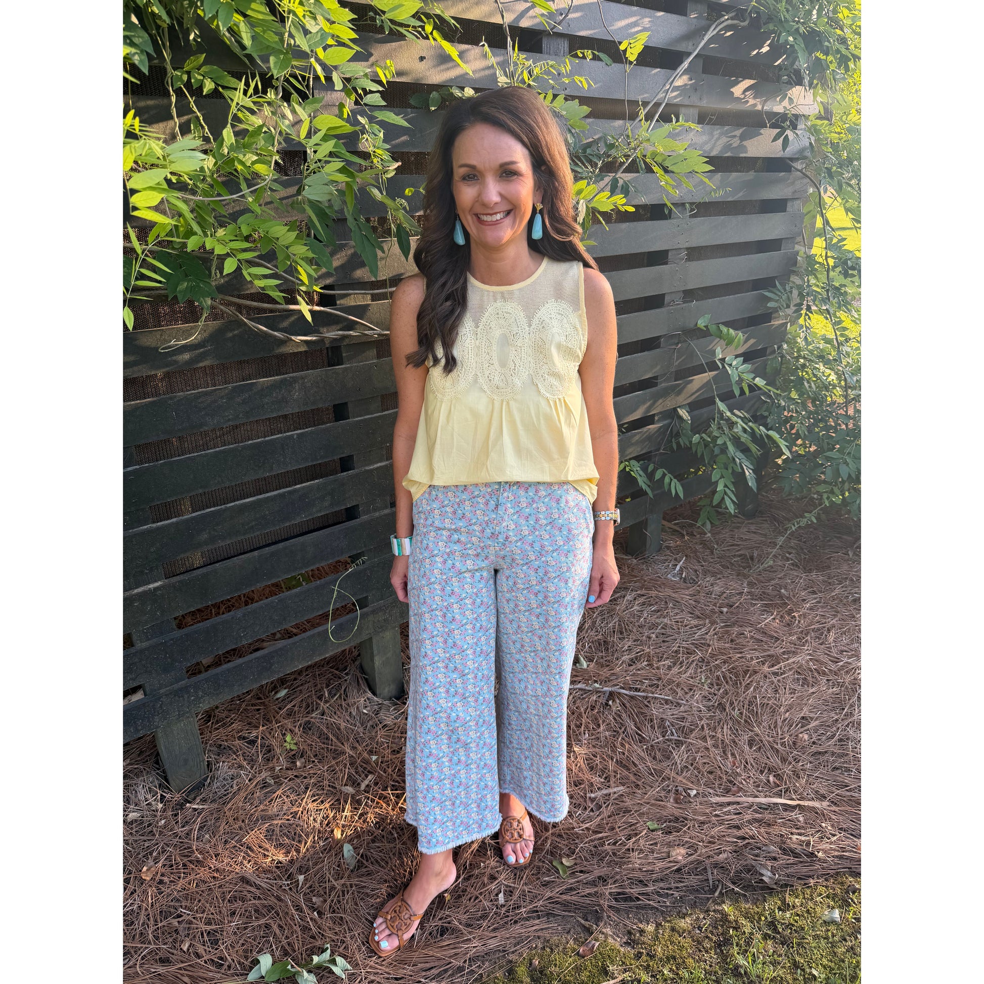 Woman standing outdoors in front of a wooden fence with greenery