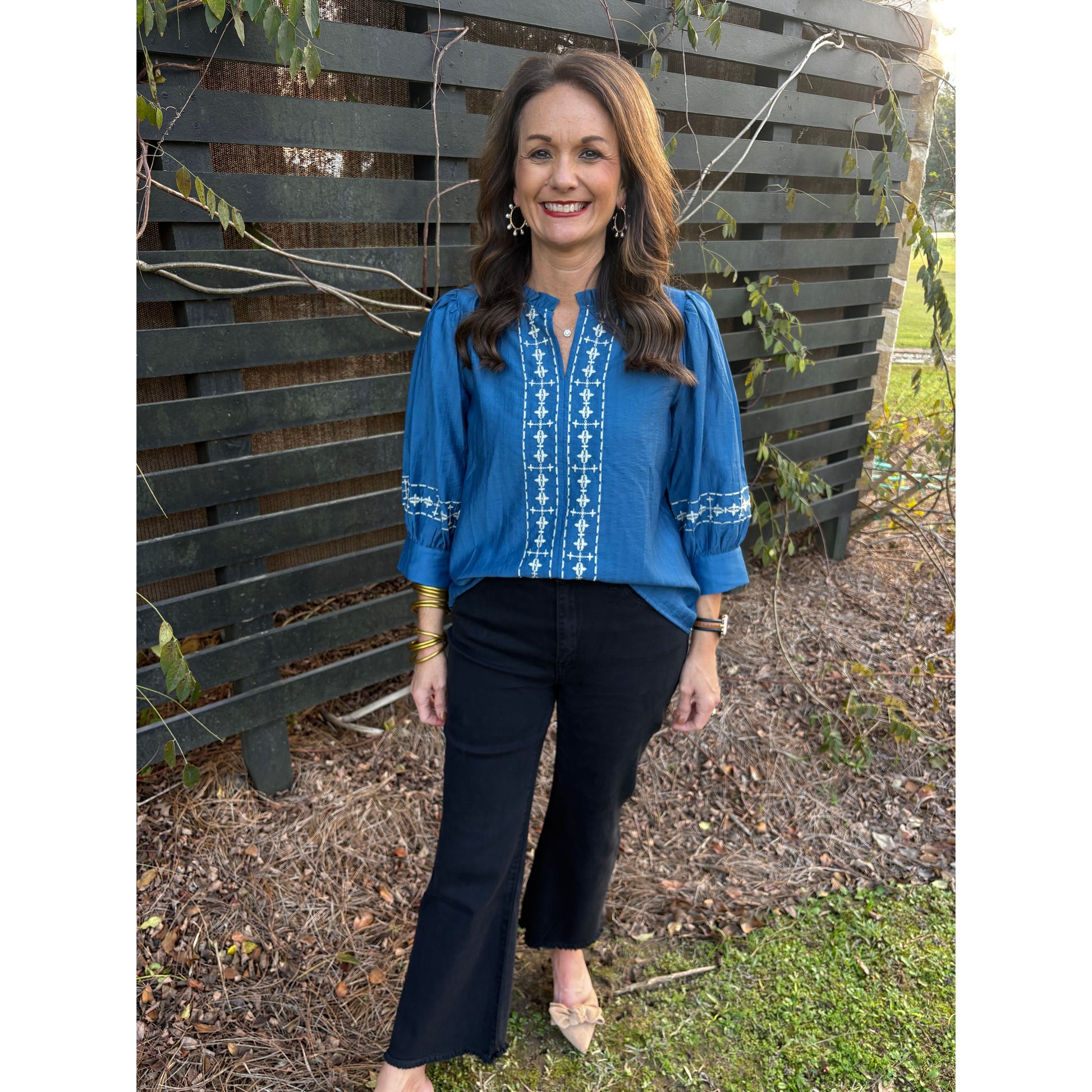 Person wearing a blue embroidered shirt and black pants standing outdoors.