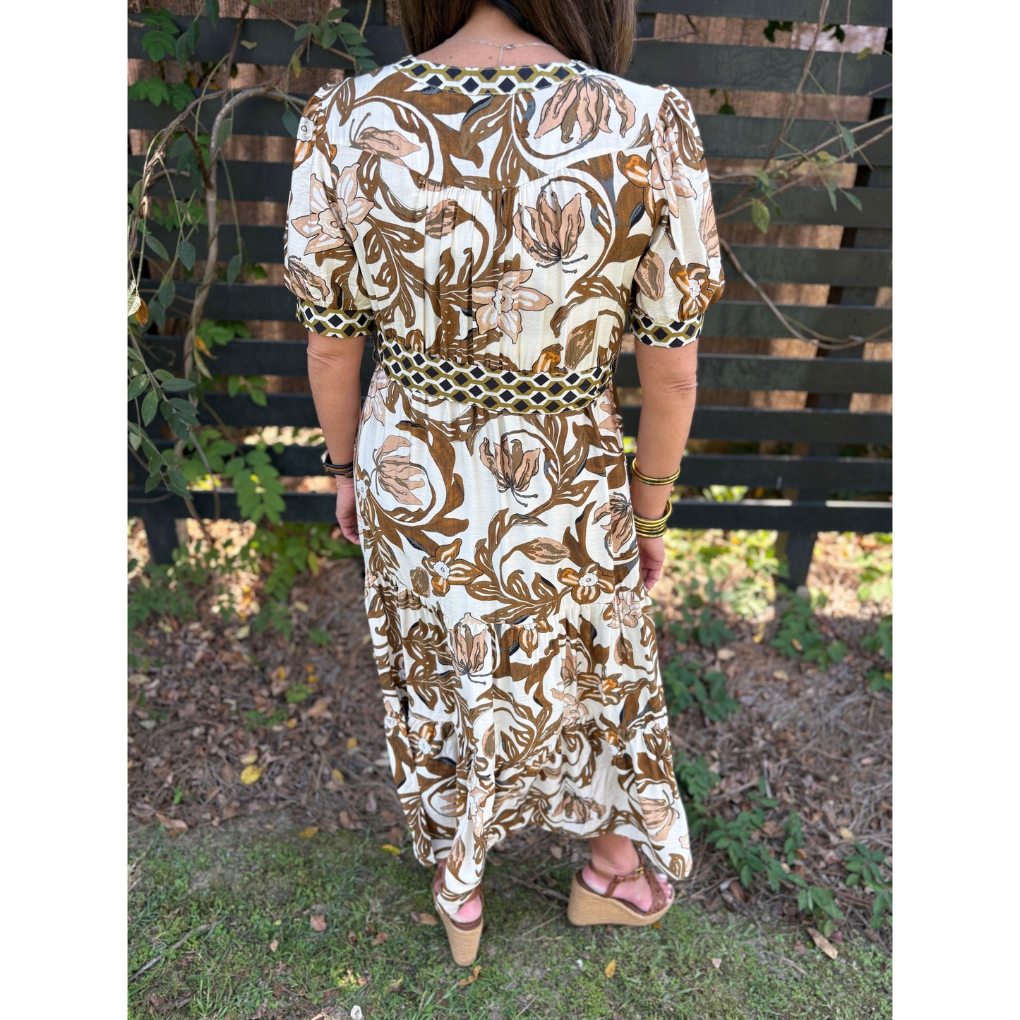 Person wearing a floral dress with a patterned back, standing outdoors.