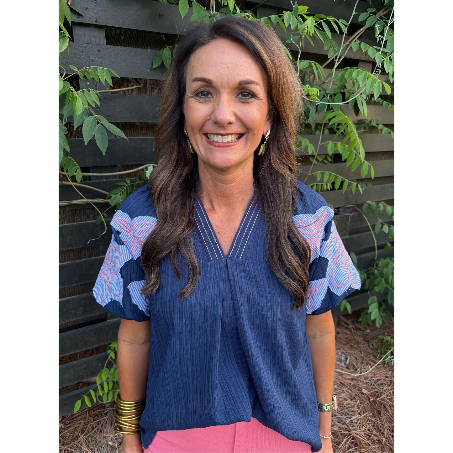 Woman wearing a blue blouse with pink accents in an outdoor setting