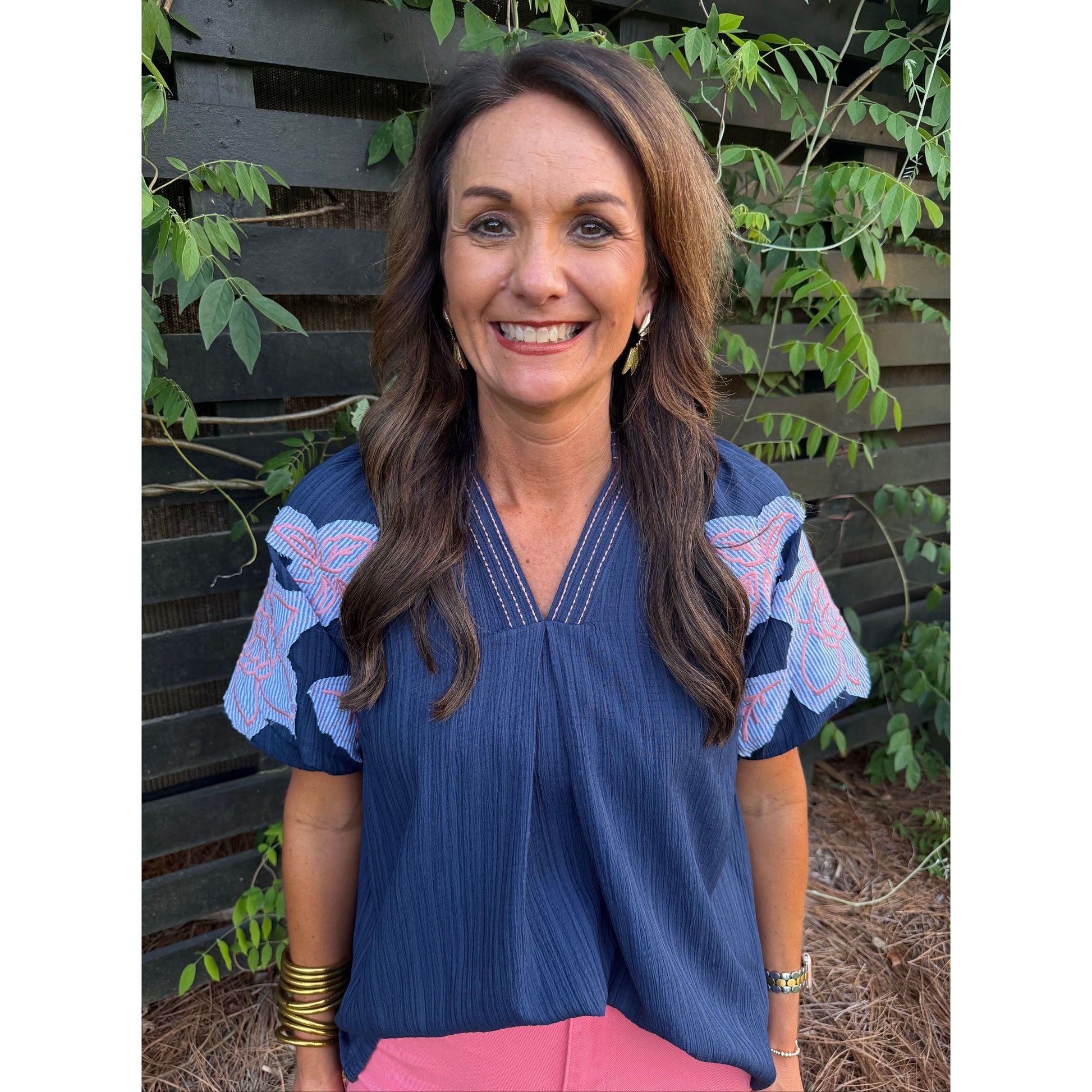 Woman wearing a blue blouse with pink accents in an outdoor setting
