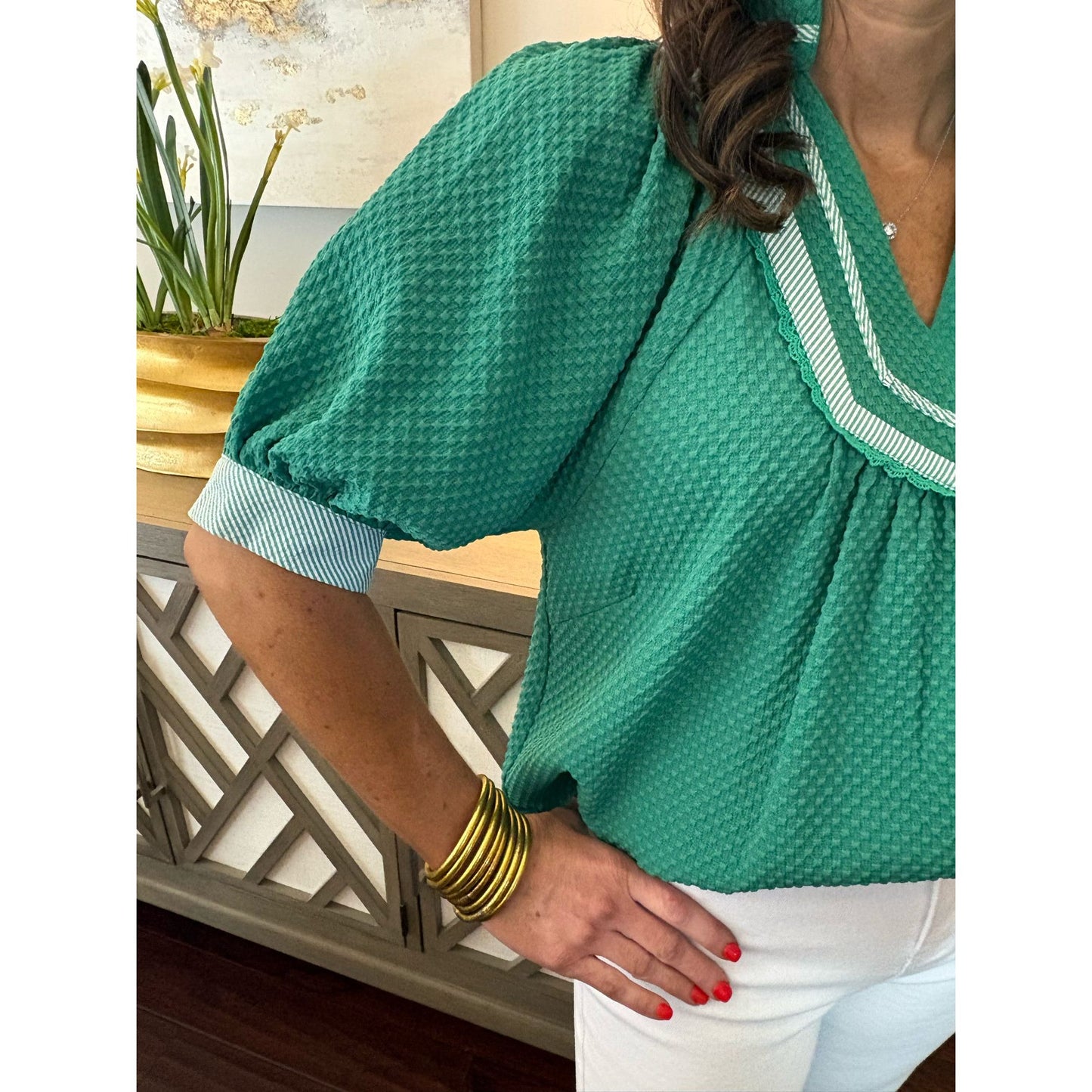 Person wearing a green textured blouse with white trim, standing indoors.