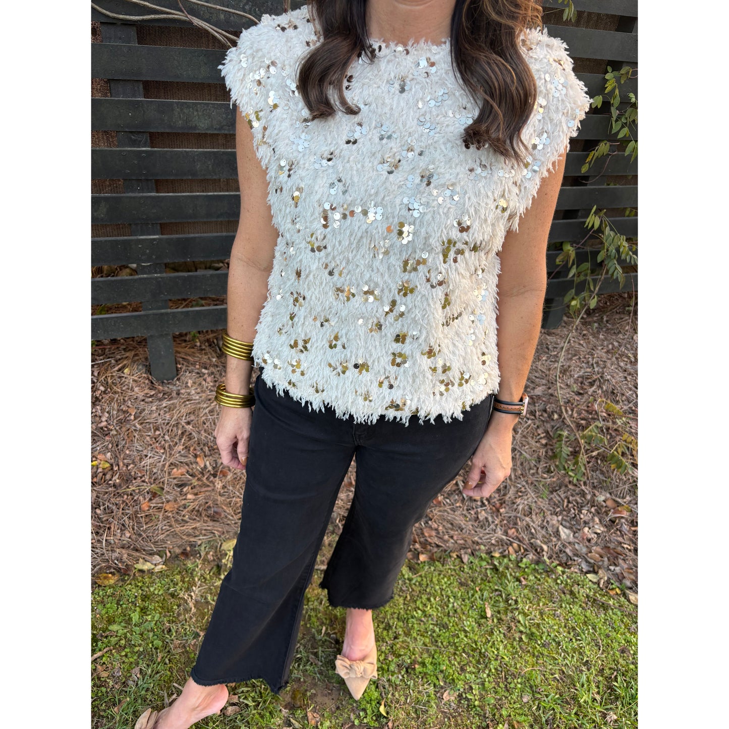 Person wearing a white sequined top and black pants on a grassy ground.