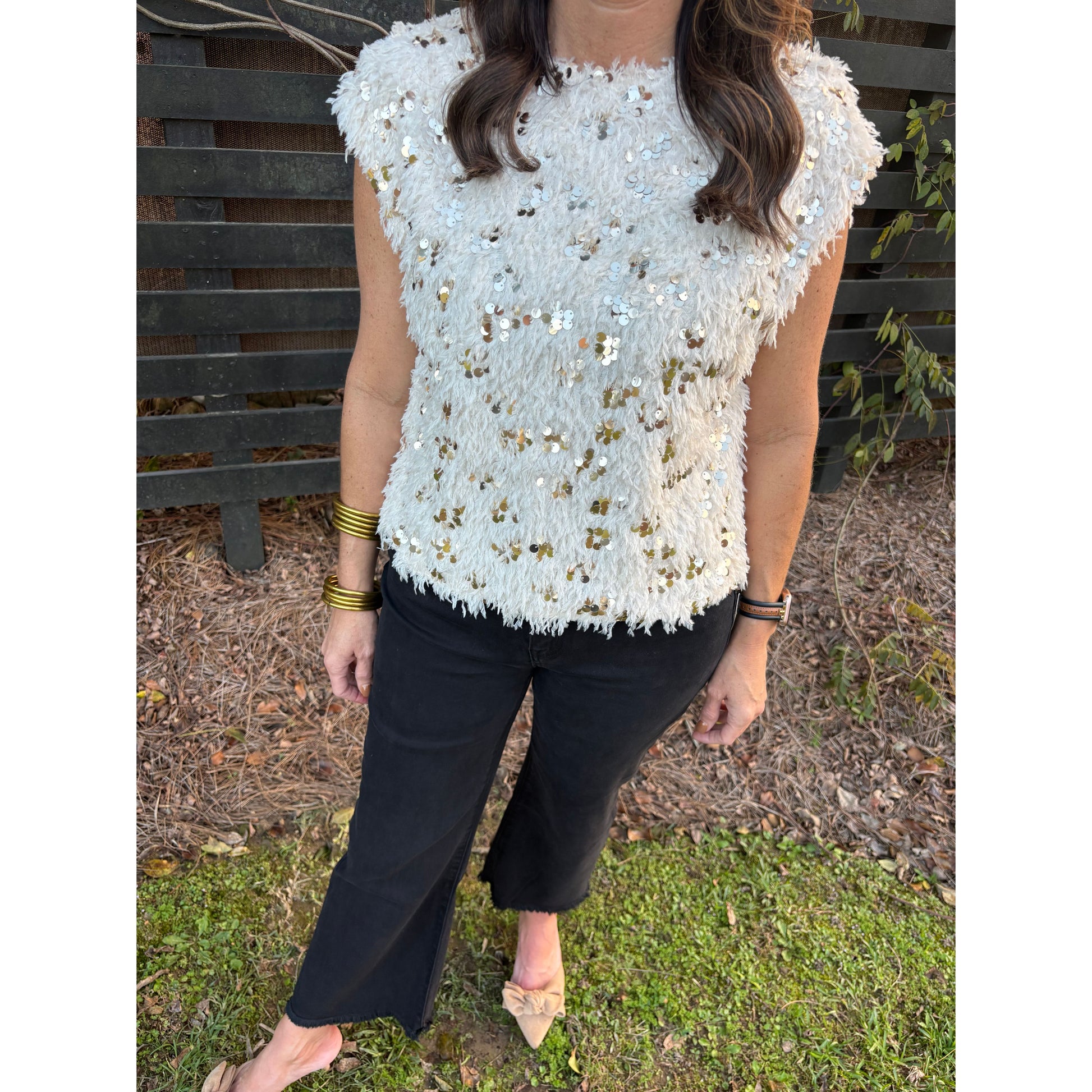 Person wearing a white sequined top and black pants on a grassy ground.