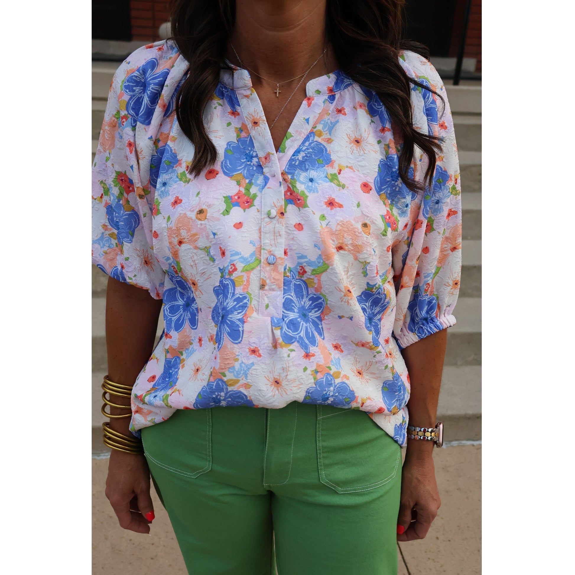 Person wearing a colorful floral dress with green pants, sitting on a white surface.