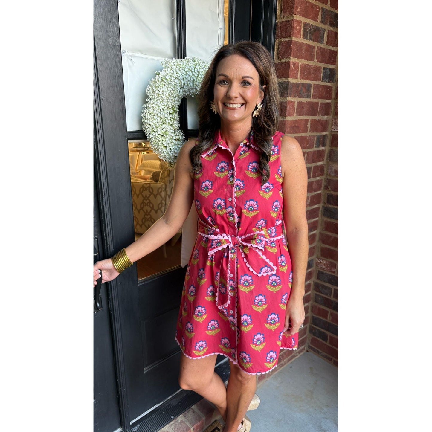 Woman in a pink floral dress standing in front of a door with a wreath.