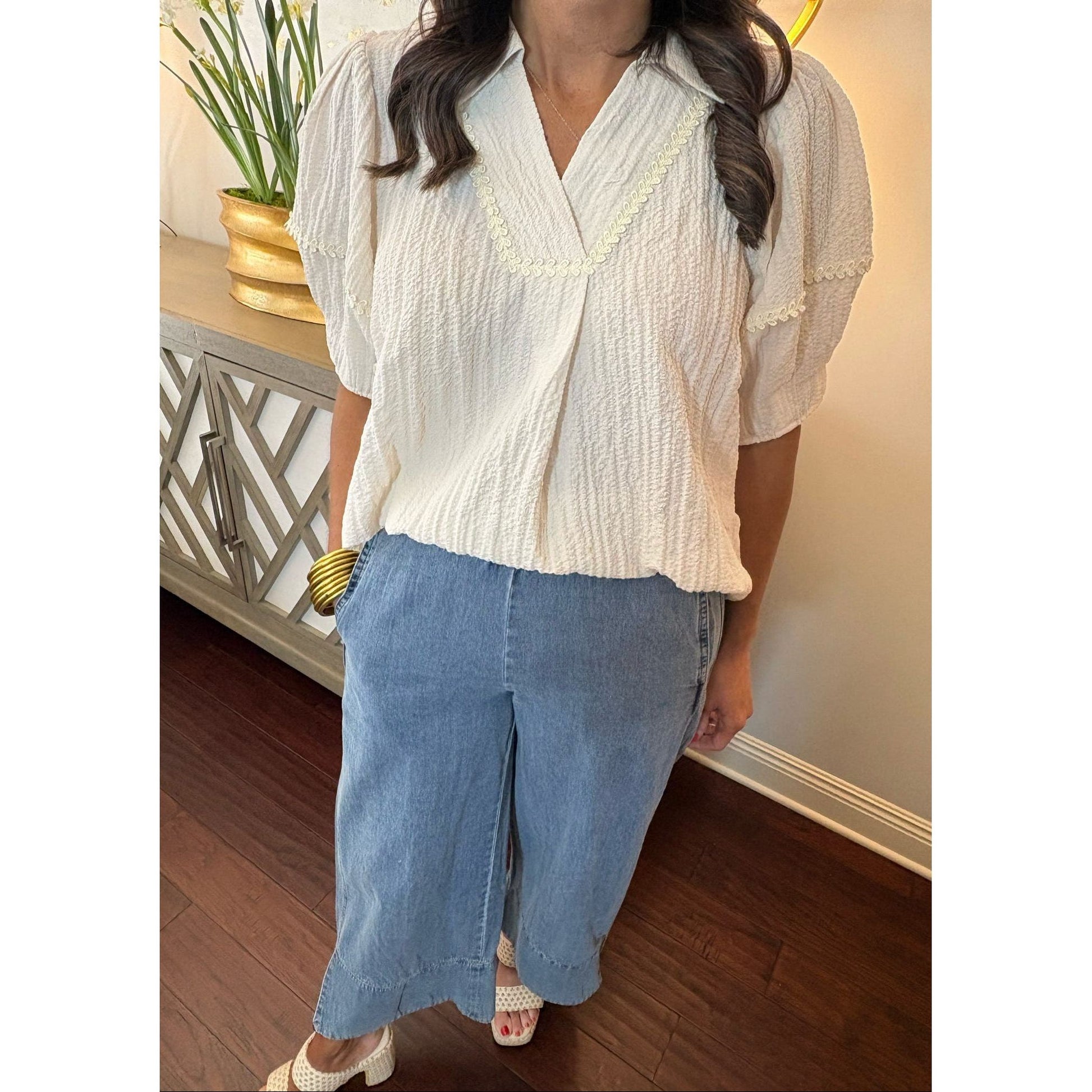 Woman wearing a white blouse and blue jeans standing indoors.