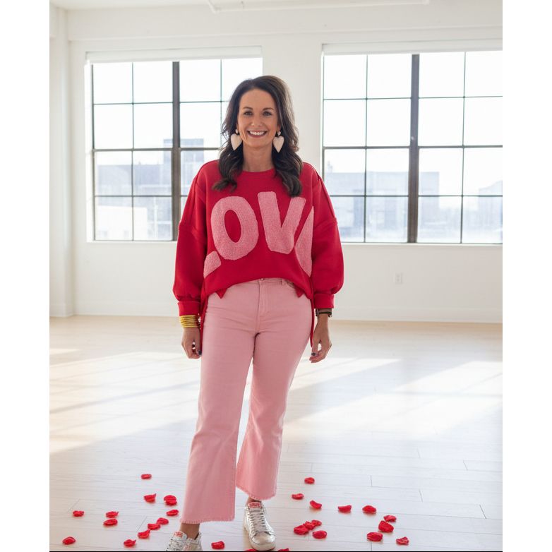 Woman wearing a red 'LOVE' sweatshirt and pink pants standing.