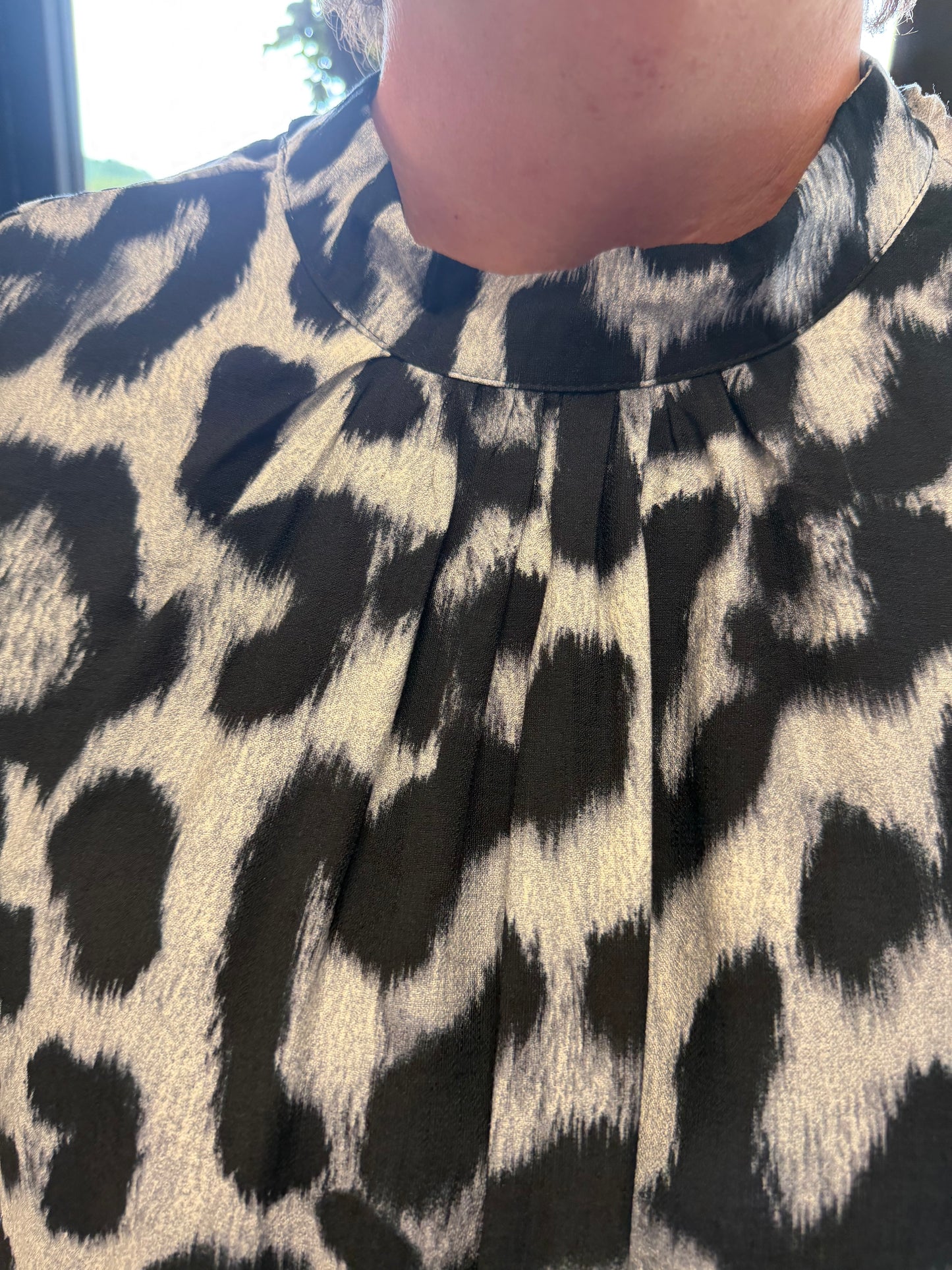 Close-up of a leopard print top with a pleated, gathered neckline, featuring black and beige spots on a textured fabric.