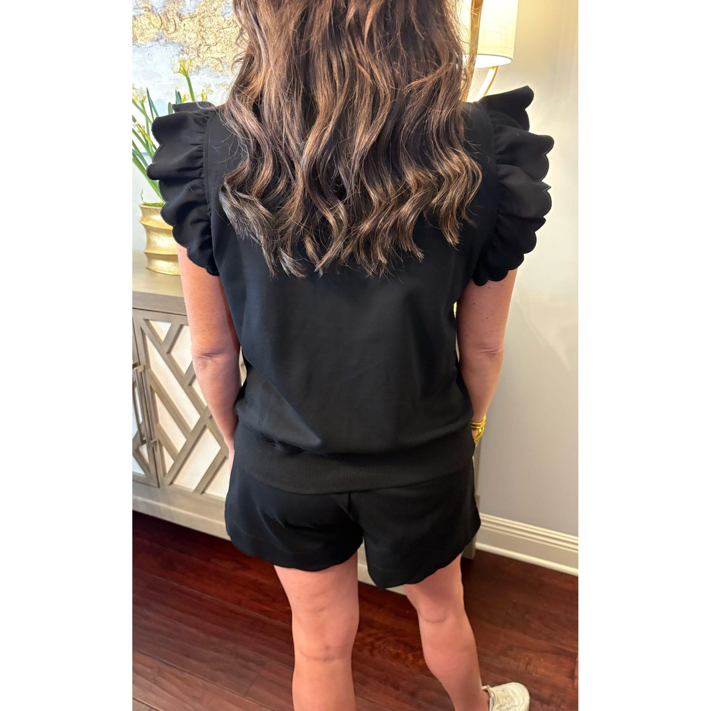 Person wearing a black outfit with ruffled sleeves in an indoor setting