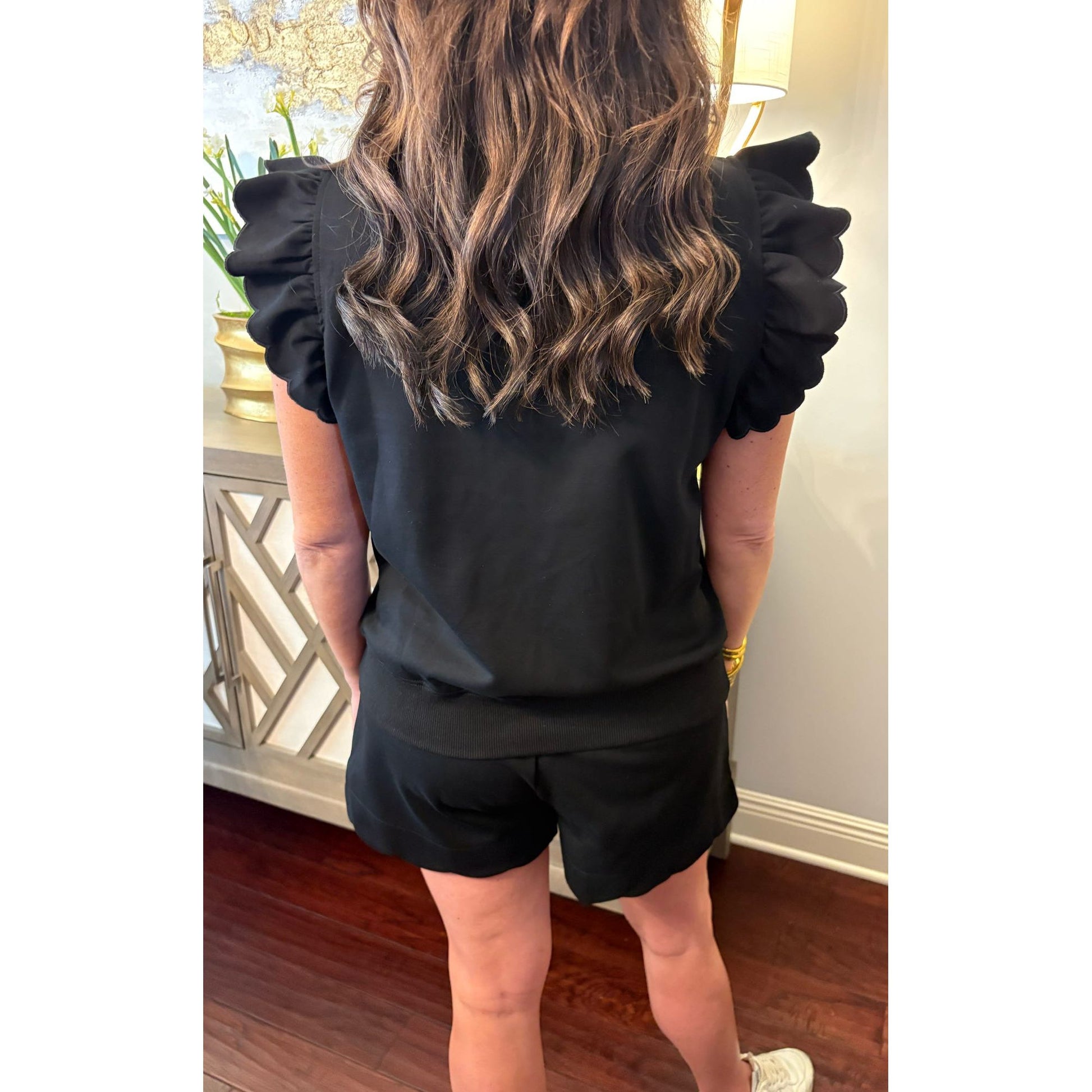 Person wearing a black outfit with ruffled sleeves in an indoor setting