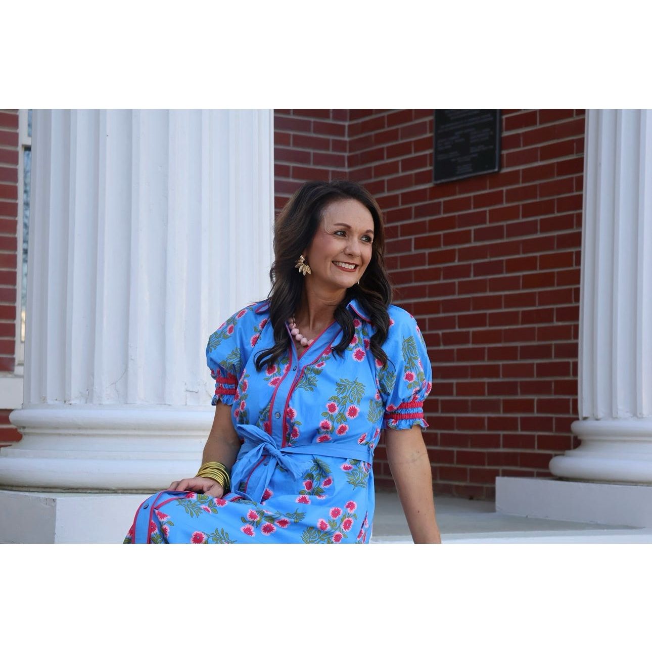 Woman in a blue floral dress sitting on steps with a brick building in the background