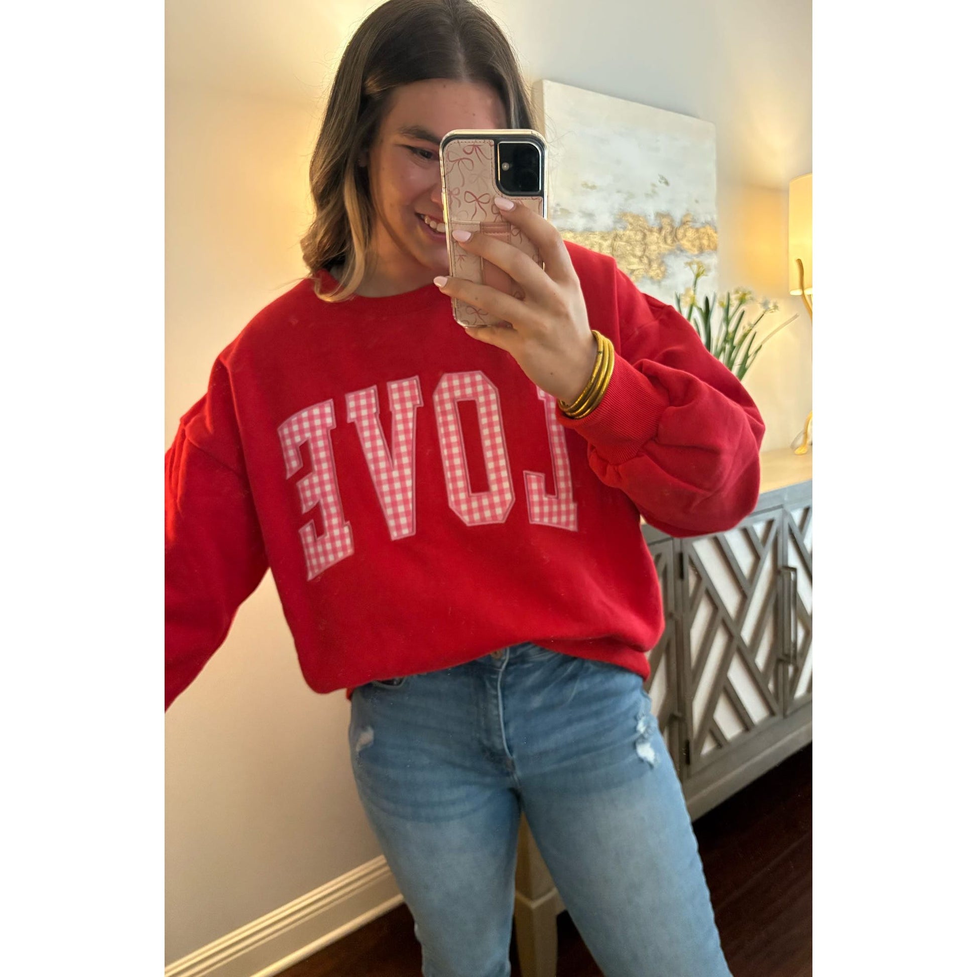 Person wearing a red sweatshirt with 'LOVE' printed on it, taking a mirror selfie.