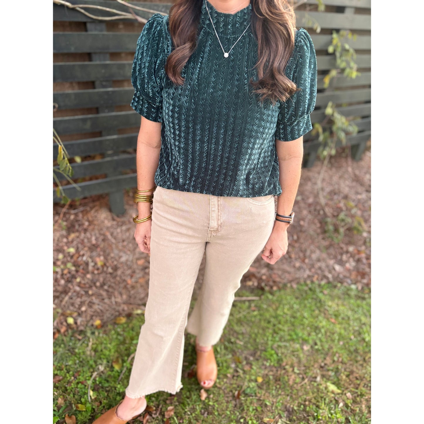 Person wearing a green patterned top and beige pants outdoors.