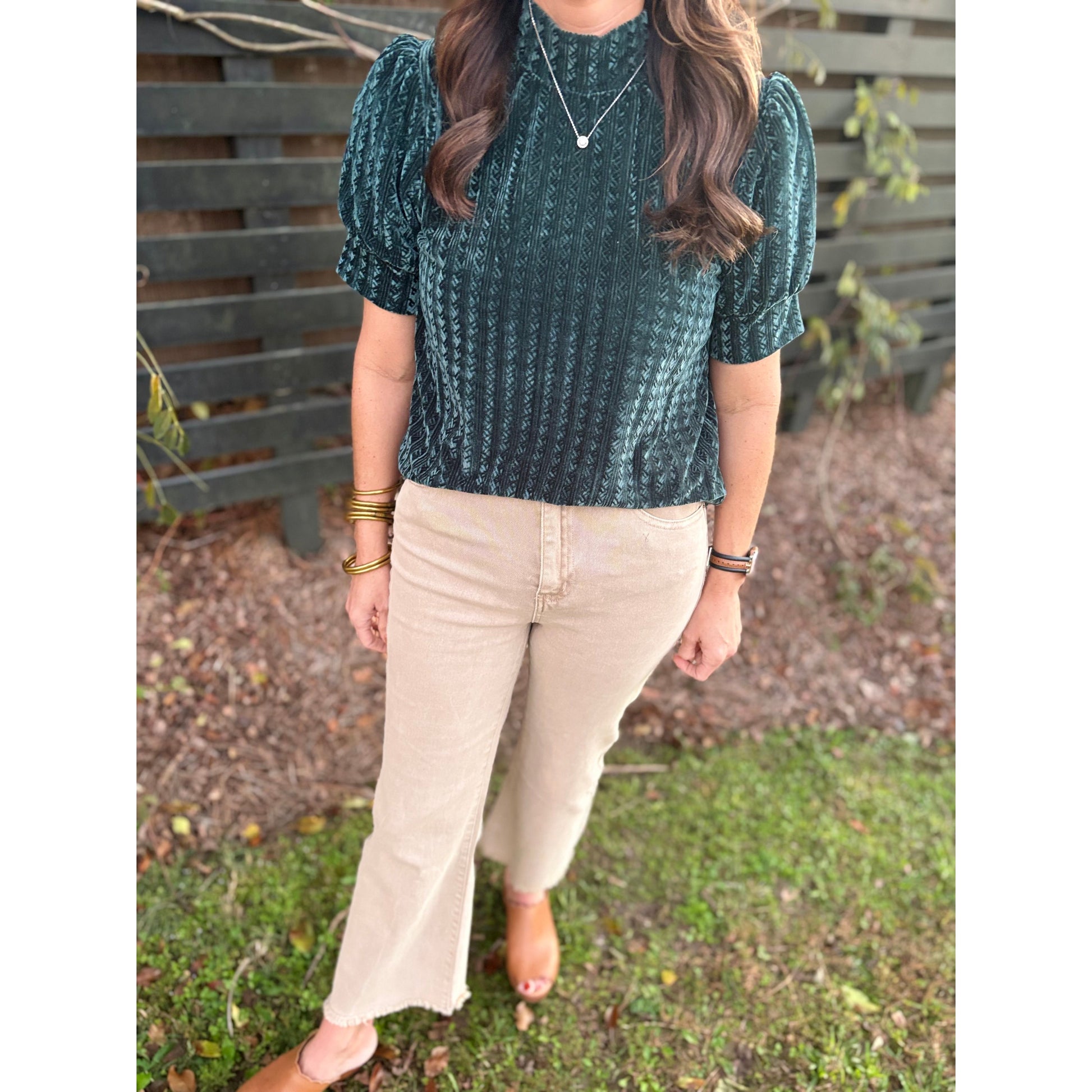 Person wearing a green patterned top and beige pants outdoors.