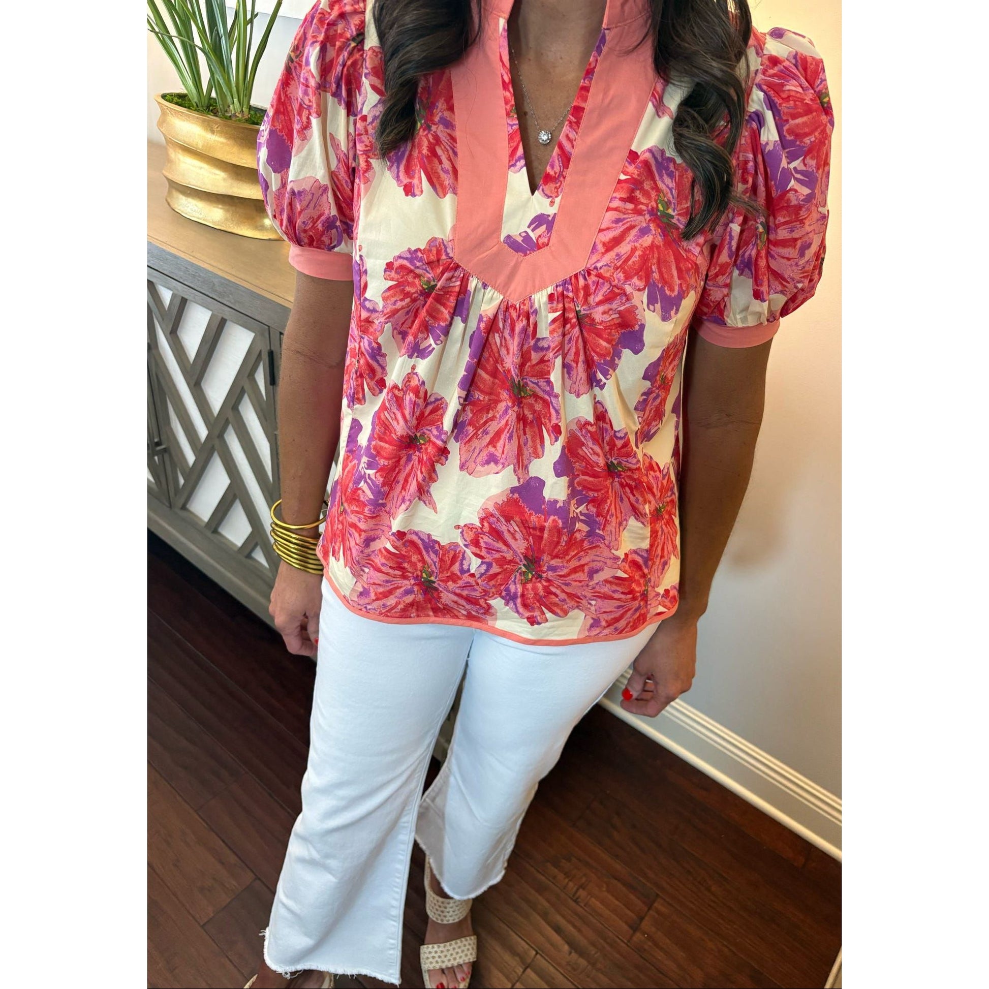 Person wearing a colorful floral blouse with white pants indoors.