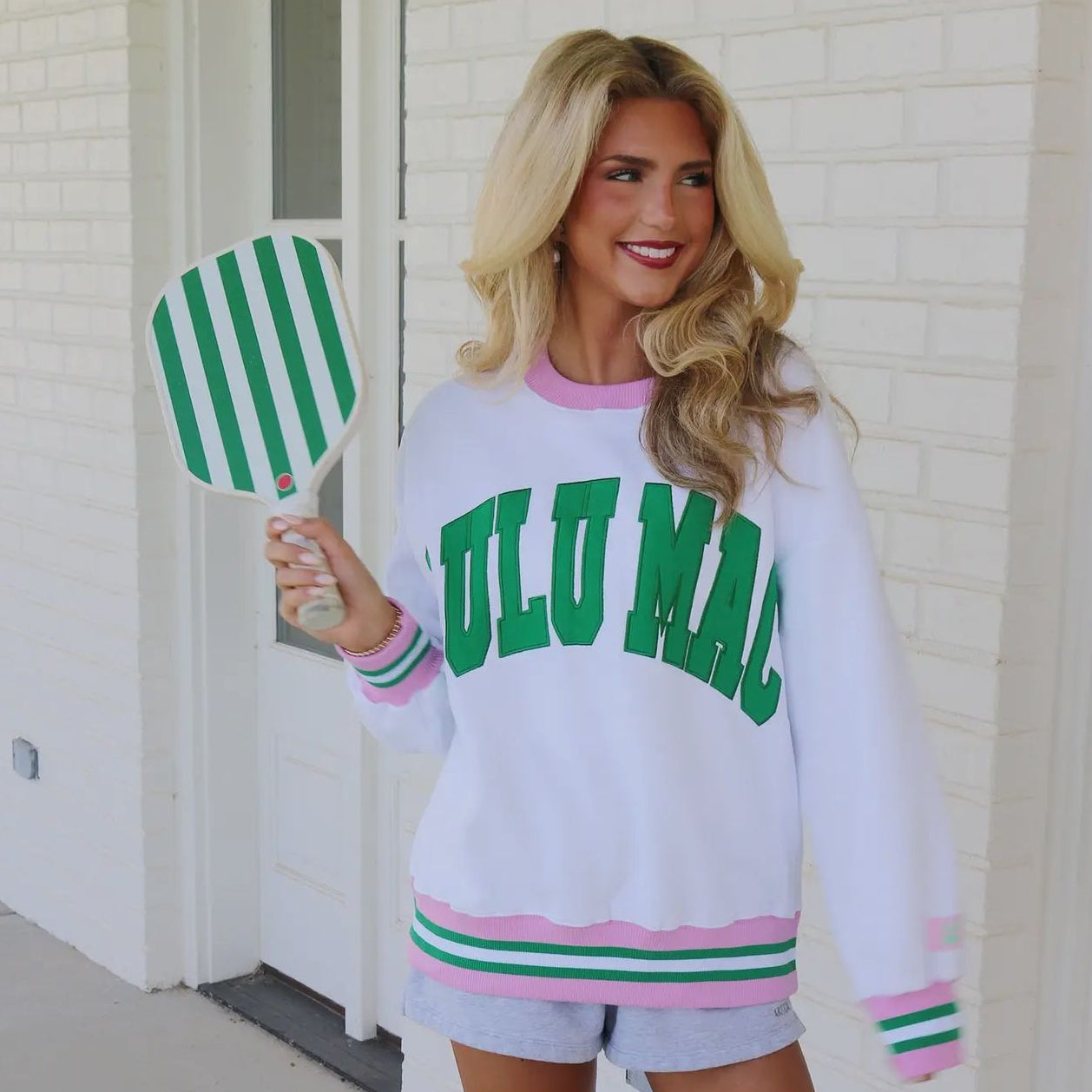Woman wearing a white sweatshirt with green text, holding a green and white striped paddle.