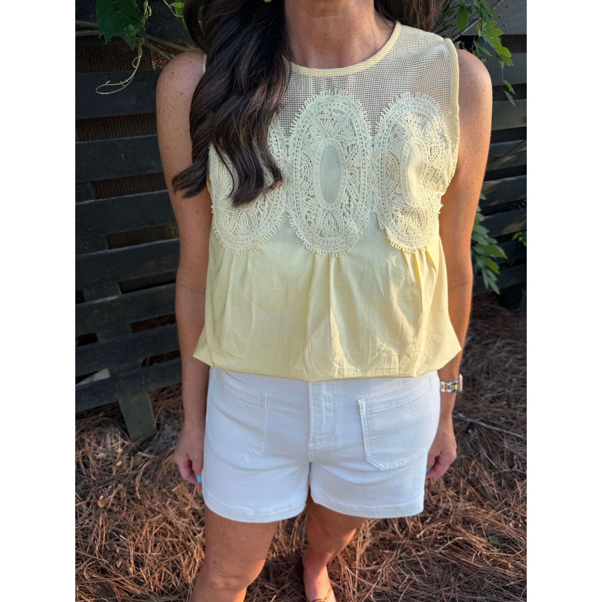 Woman wearing a light yellow lace top and white shorts outdoors.