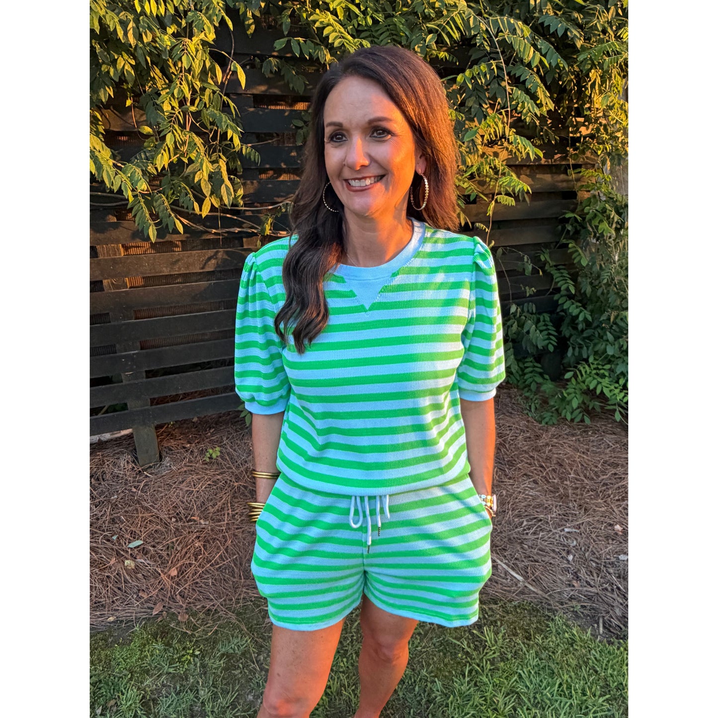 Woman wearing a green and white striped outfit sitting outdoors.