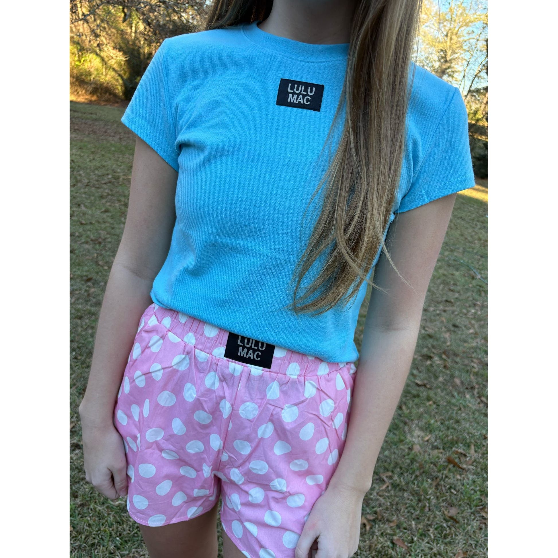 Person wearing a blue Lulu Mac t-shirt and pink shorts with white polka dots outdoors.