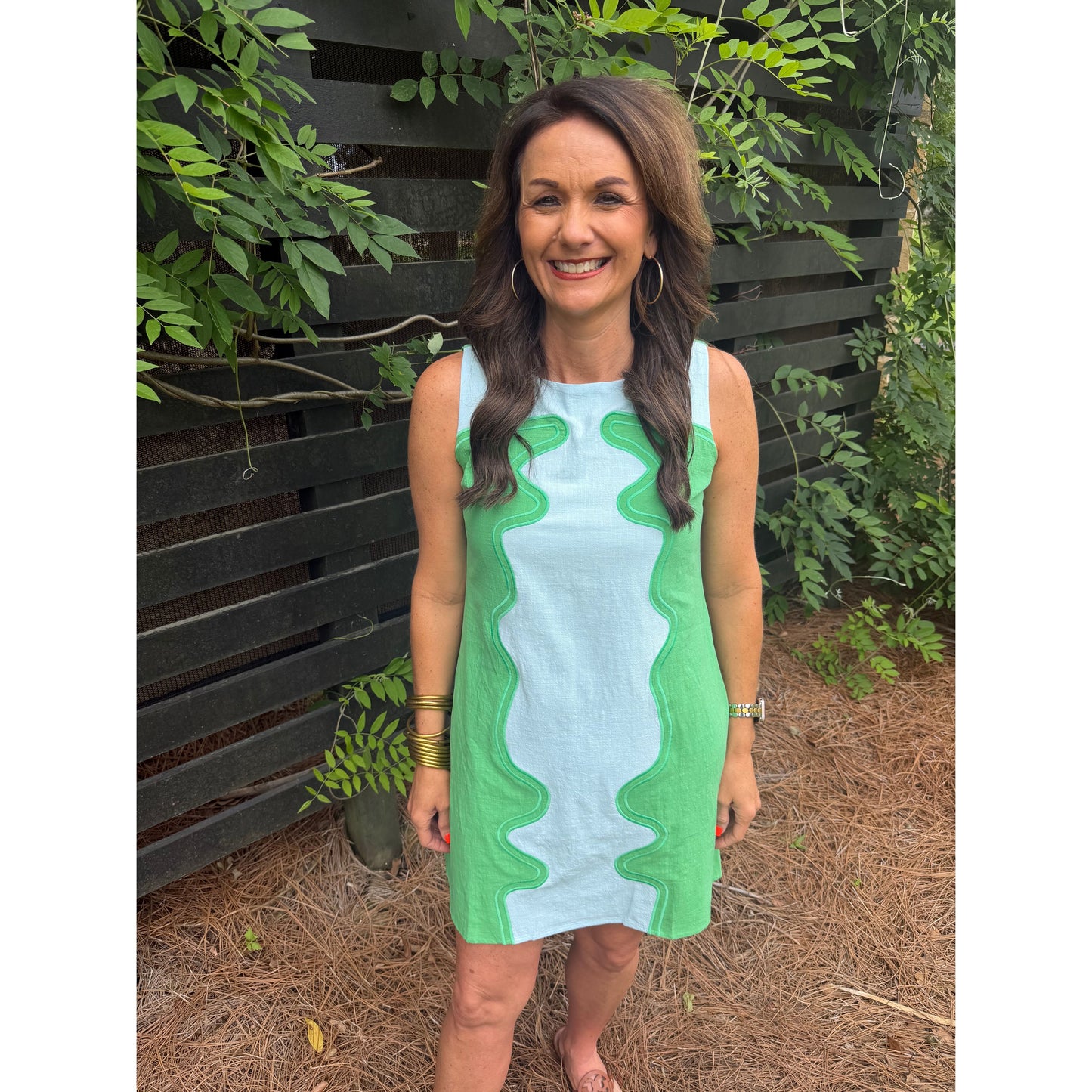 Woman wearing a green and white dress standing outdoors with greenery in the background