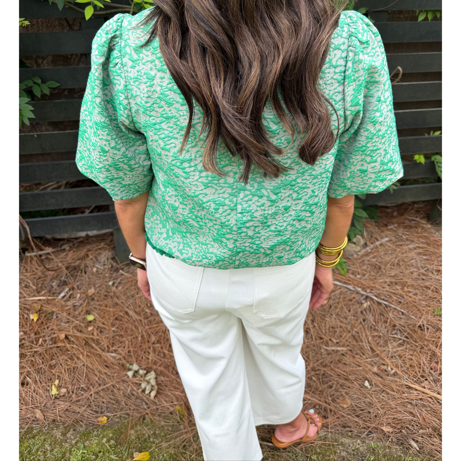 Person wearing a green floral jacket and white pants outdoors.